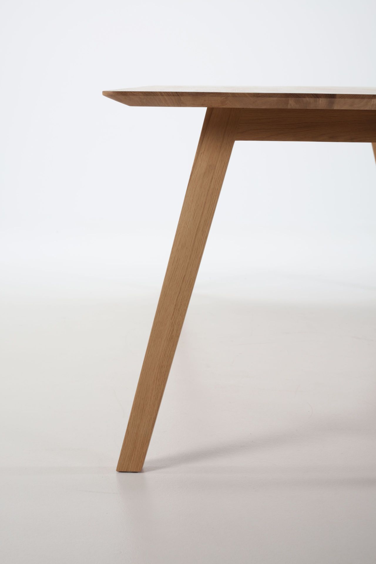 Detailaufnahme vom Prostoria Monk Tisch: Tischplatte und Tischbein aus hellem Holz vor weißem Hintergrund.