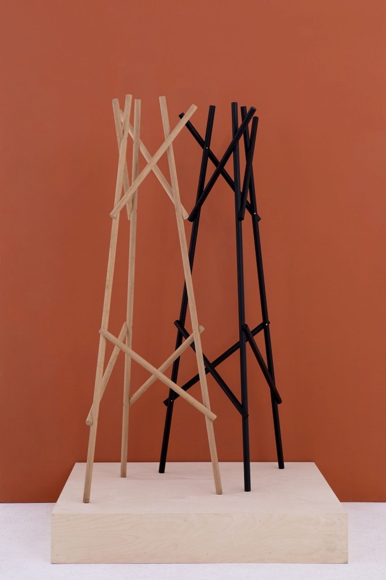 Kendo Garderobenständer von Cascando in Schwarz und Naturholz auf einem Holzpodest vor orangefarbenem Hintergrund.