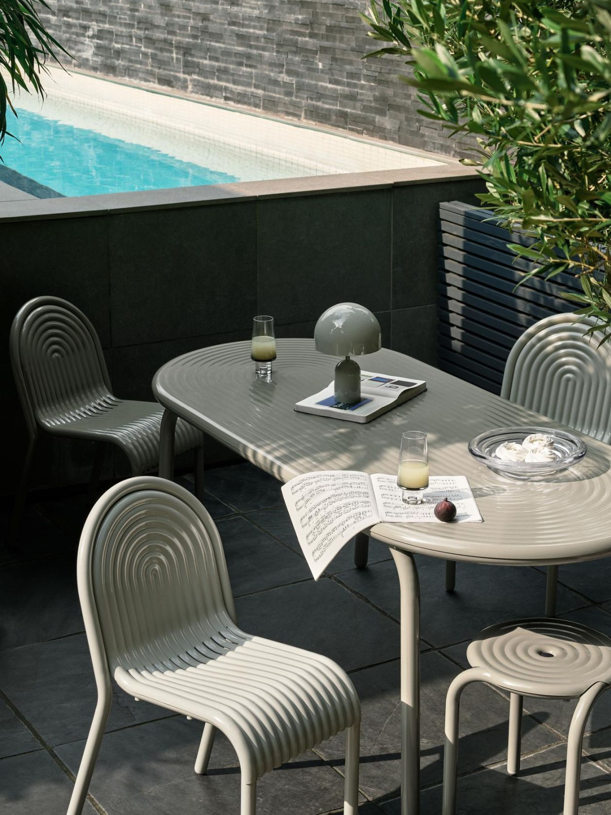Groove Outdoor Tisch von Tom Dixon in Putty mit Stühlen und Lampe im Garten.