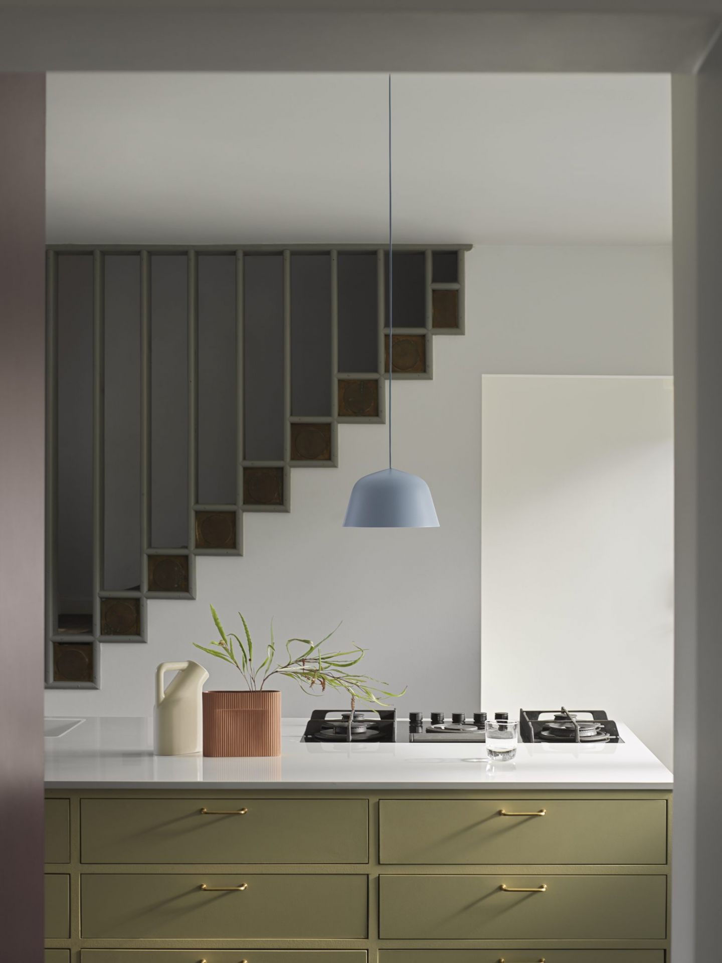 Helle Küche mit blauer Ambit Pendelleuchte von Muuto über Kochfeld und Kücheninsel.