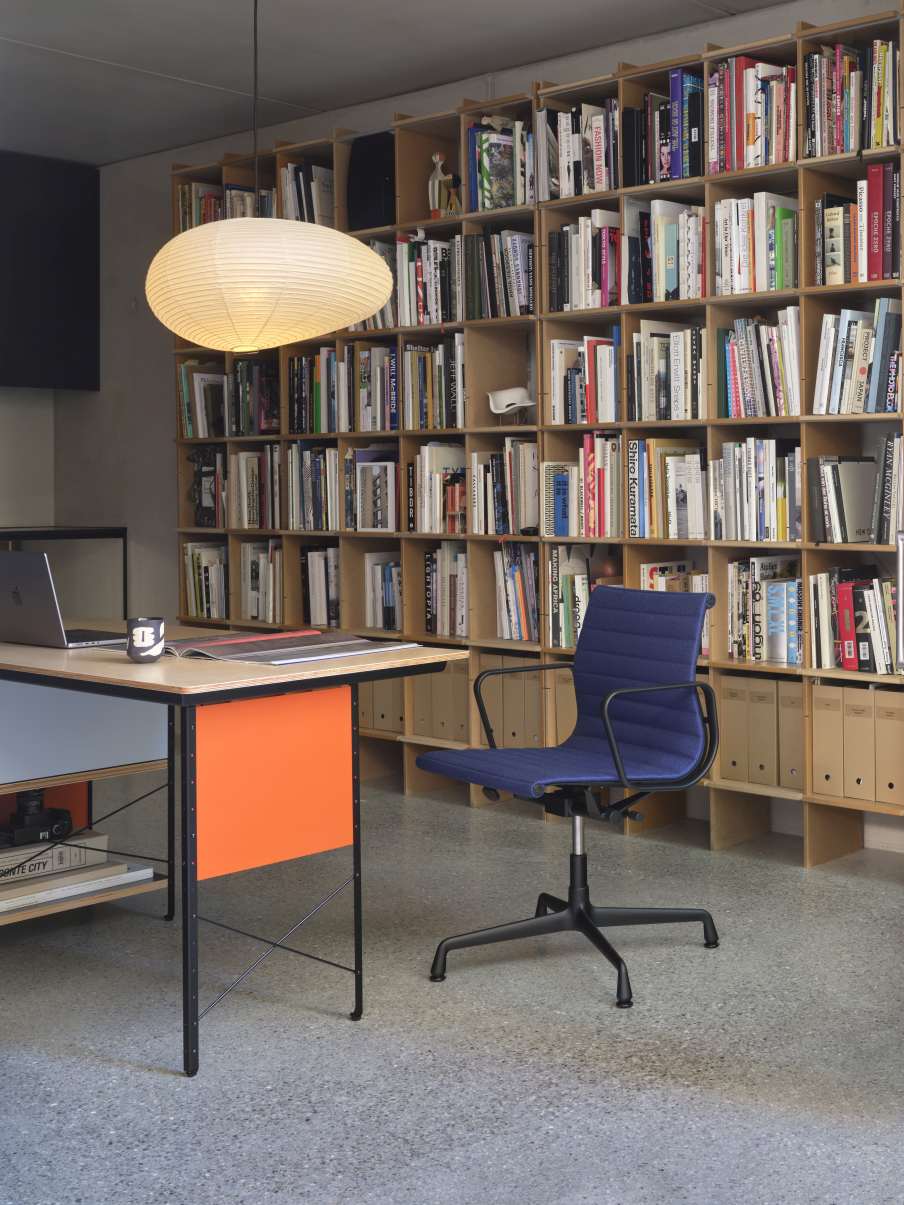 Blauer Vitra Aluminium Chair EA 132 Bürostuhl vor Bücherregal und Schreibtisch.