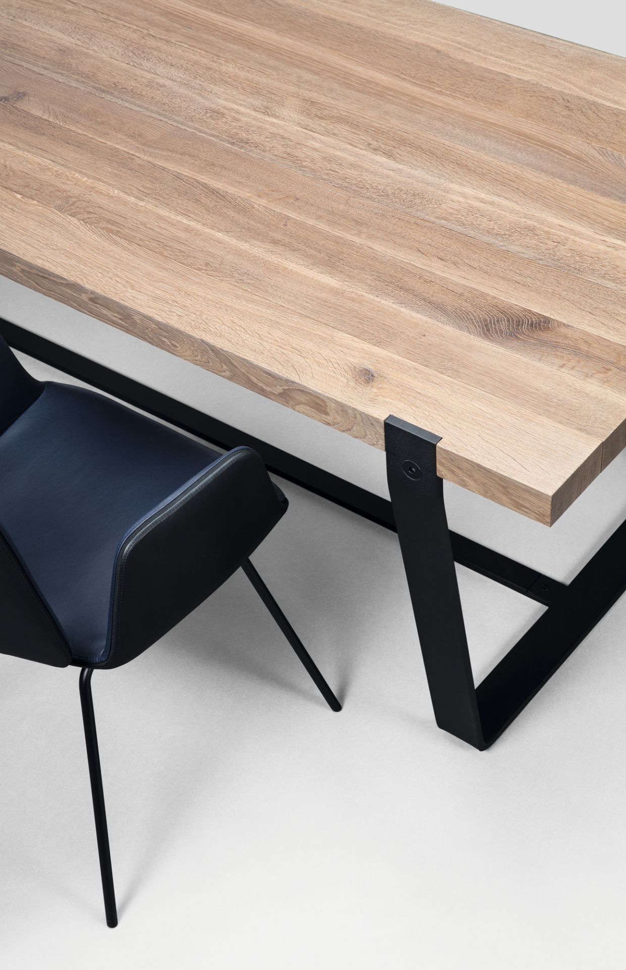 Detailaufnahme von Janua BB 11 Clamp Tisch mit Eichenholzplatte und schwarzem Metallgestell, dazu ein blauer Stuhl.