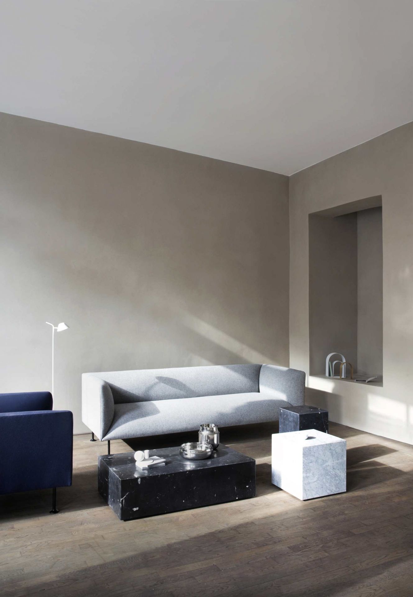 Wohnzimmer mit grauem Sofa, blauem Sessel und Audo Copenhagen Plinth Tisch aus Marmor in Schwarz und Weiß.