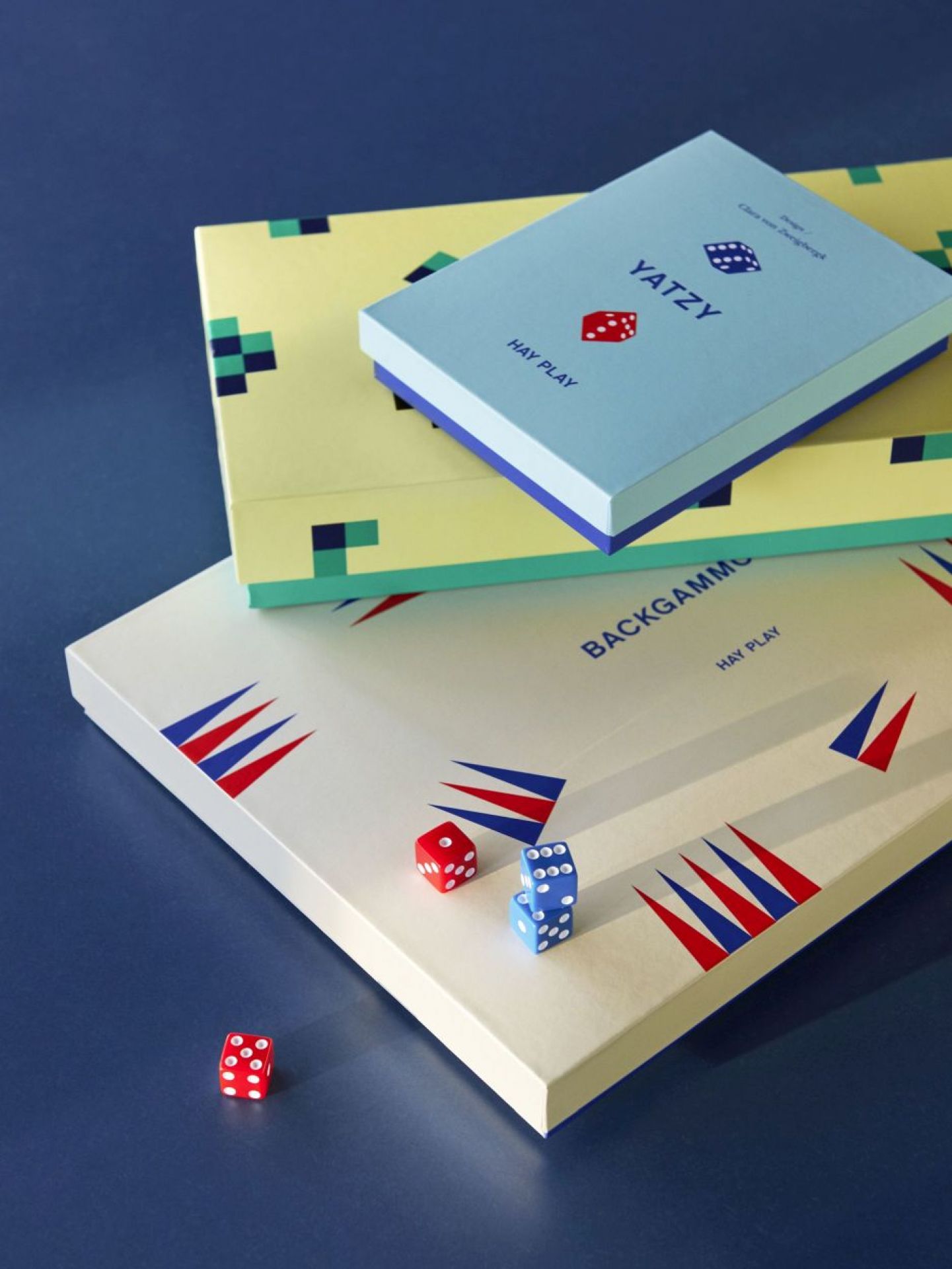 Stapel aus Hay Play Brettspielen, inklusive Play Yatzy DE Blau, mit Würfeln auf blauem Hintergrund.