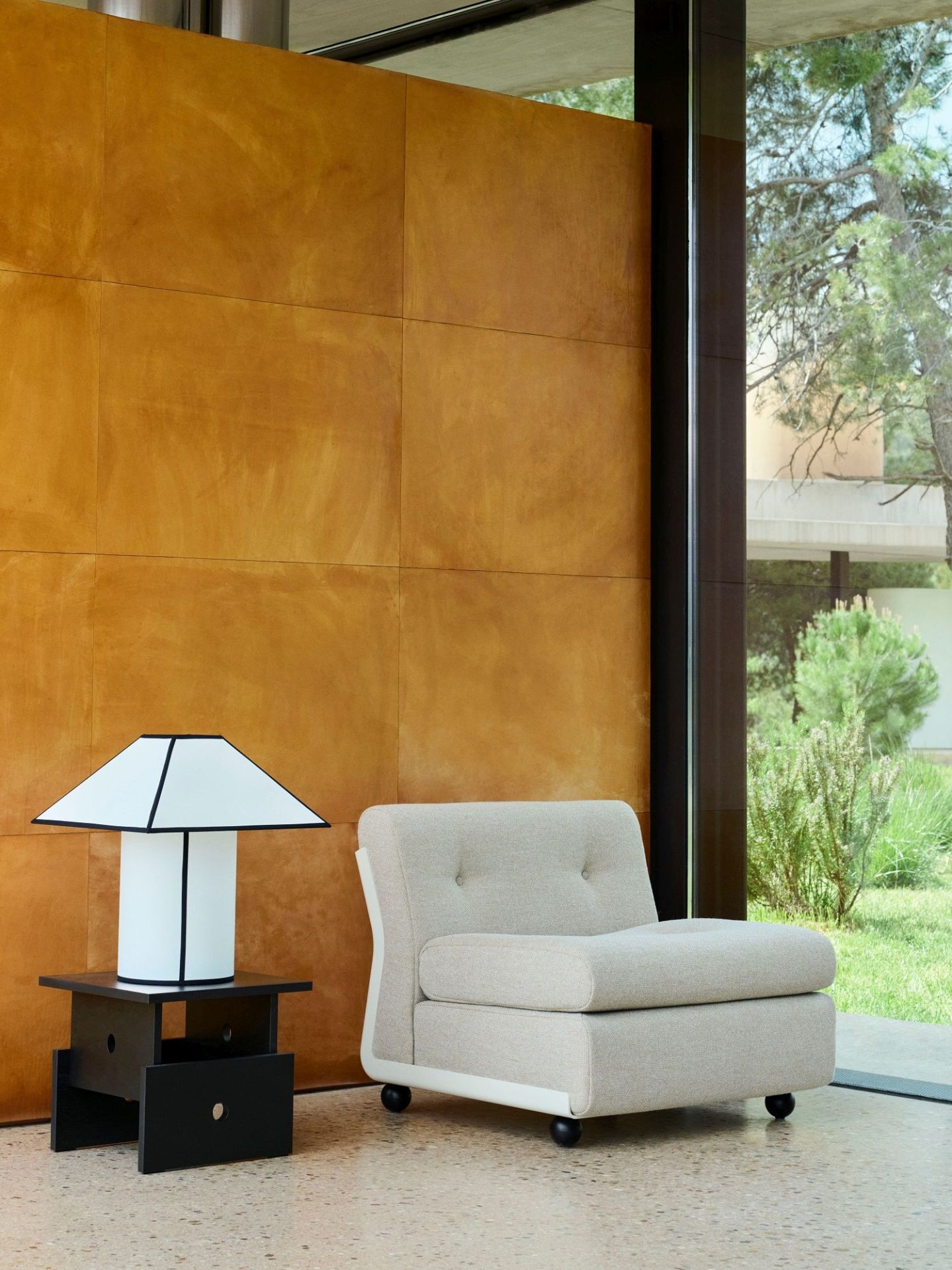Ava Pyramid Table Lamp von Hay auf schwarzem Nachttisch neben beigem Sessel, modernes Wohnambiente.