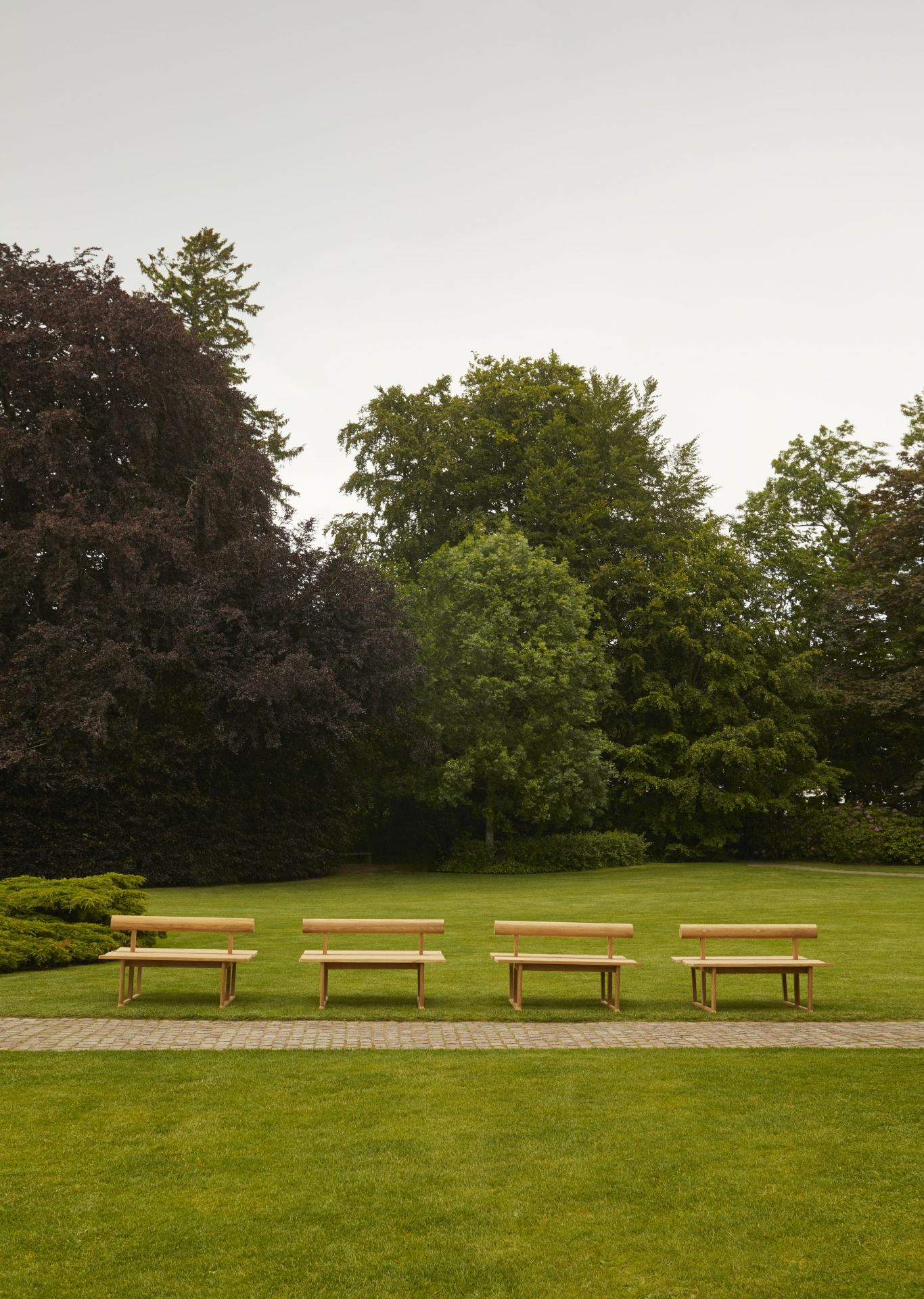 Vier Skagerak Banco Teak Bänke im Freien auf Rasen. Outdoor Möbel für Garten und Terrasse.