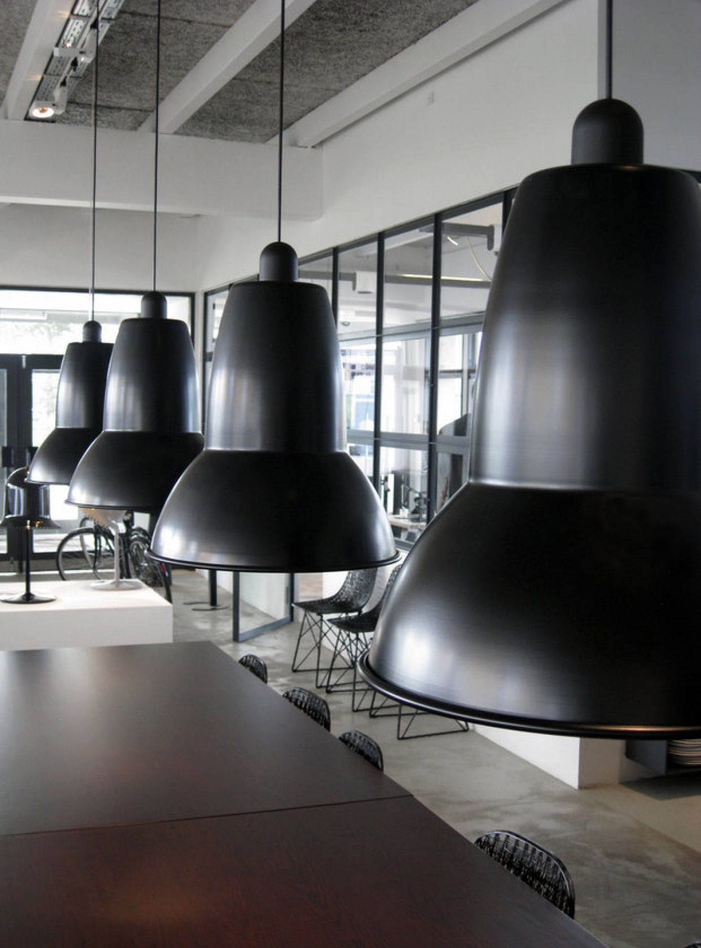 Schwarze Anglepoise Original 1227 Giant Pendelleuchten hängen über einem langen Holztisch in einem modernen Büro.