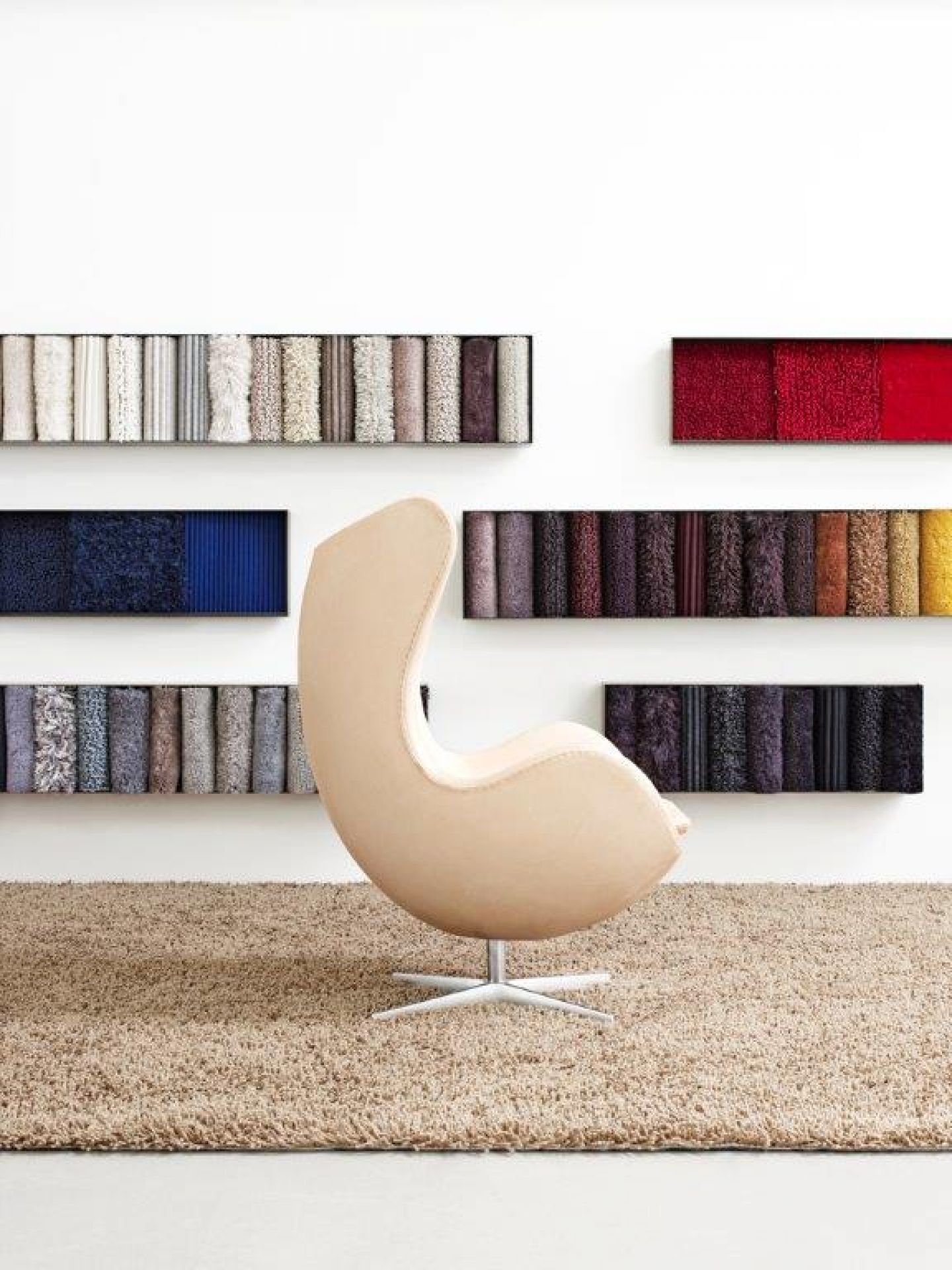 Beiger Egg Chair Hocker von Fritz Hansen auf beigem Teppich vor Wand mit Stoffmustern.