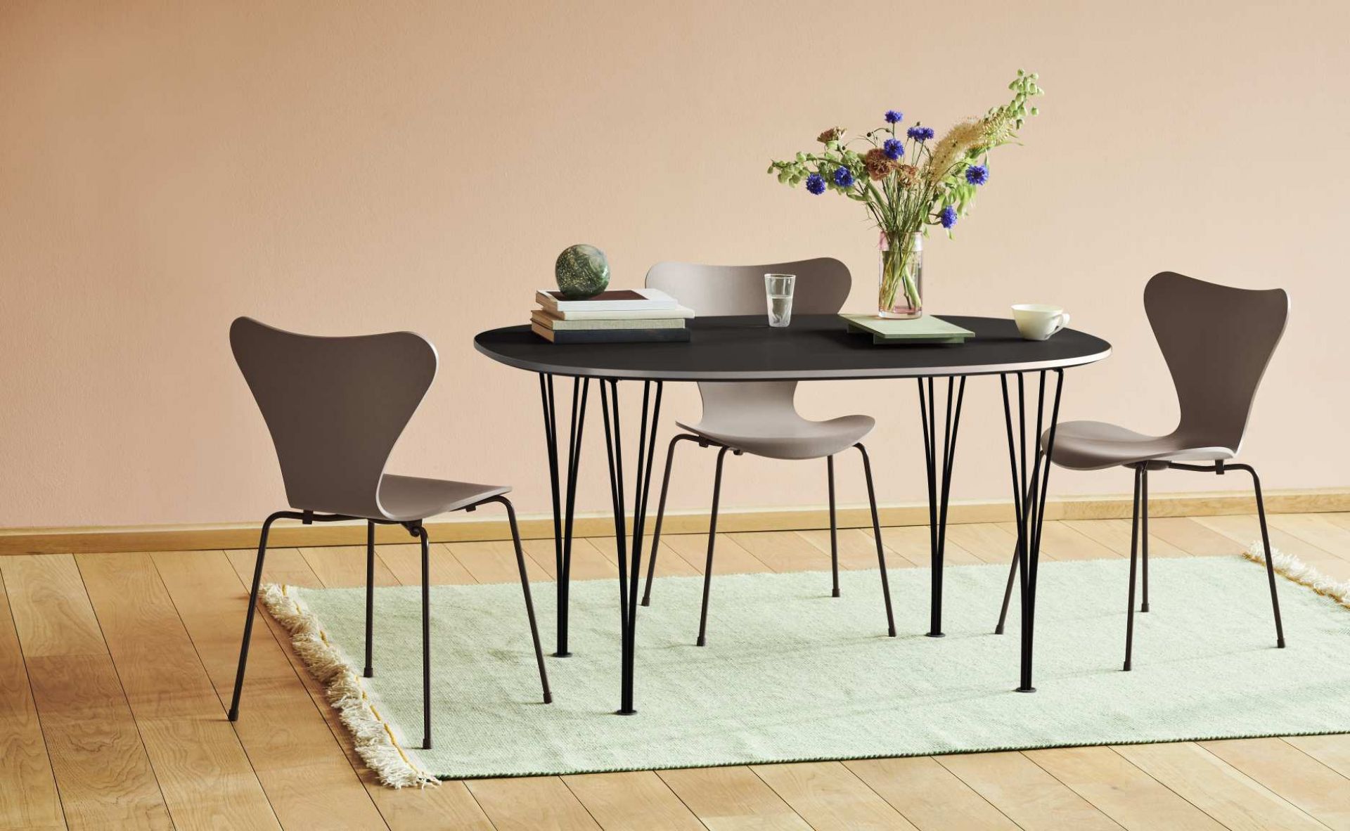 Fritz Hansen Super Elliptisch Esstisch mit Stühlen, schwarze Tischplatte und Blumen auf mintfarbenem Teppich.