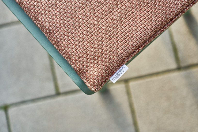 Detailaufnahme der Weishäupl Vapio Bank Outdoor Sitzfläche mit rot-beige gemustertem Stoff und Markenlabel.