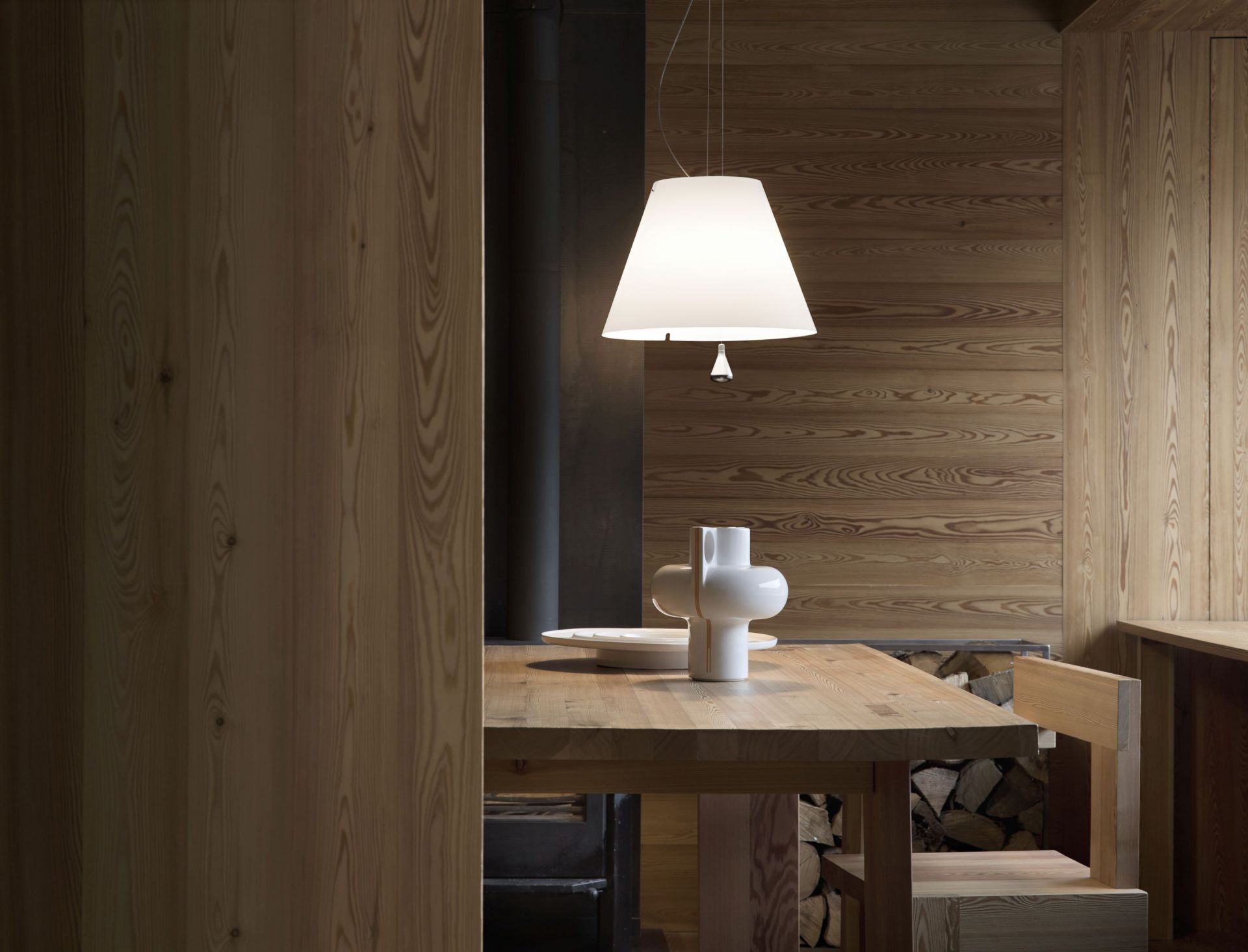 Helle Costanza Stehleuchte von Luceplan über Esstisch mit Holzstuhl und Holzwand.