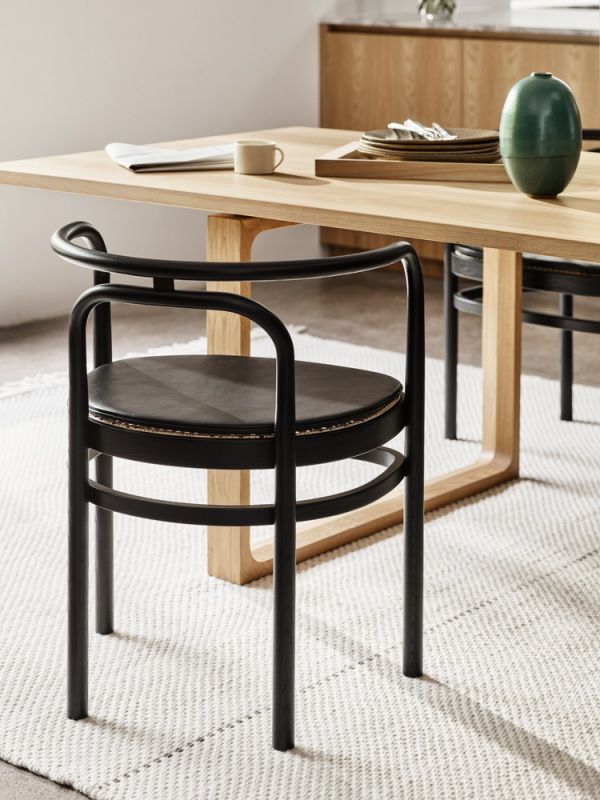 Schwarzer PK 15 Stuhl von Fritz Hansen am Esstisch auf einem Teppich. Designstuhl mit Leder.