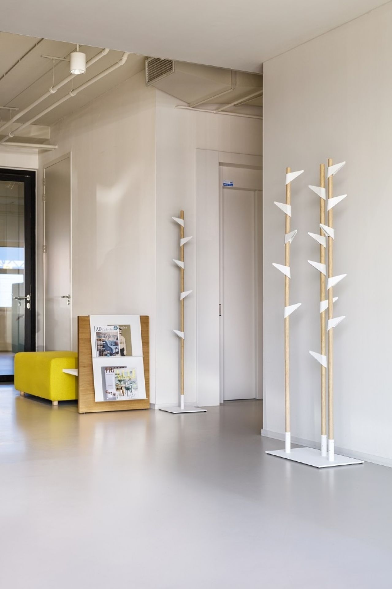Cascando Bamboo Standgarderobe aus Holz mit weißen Haken in einem modernen Büroflur.