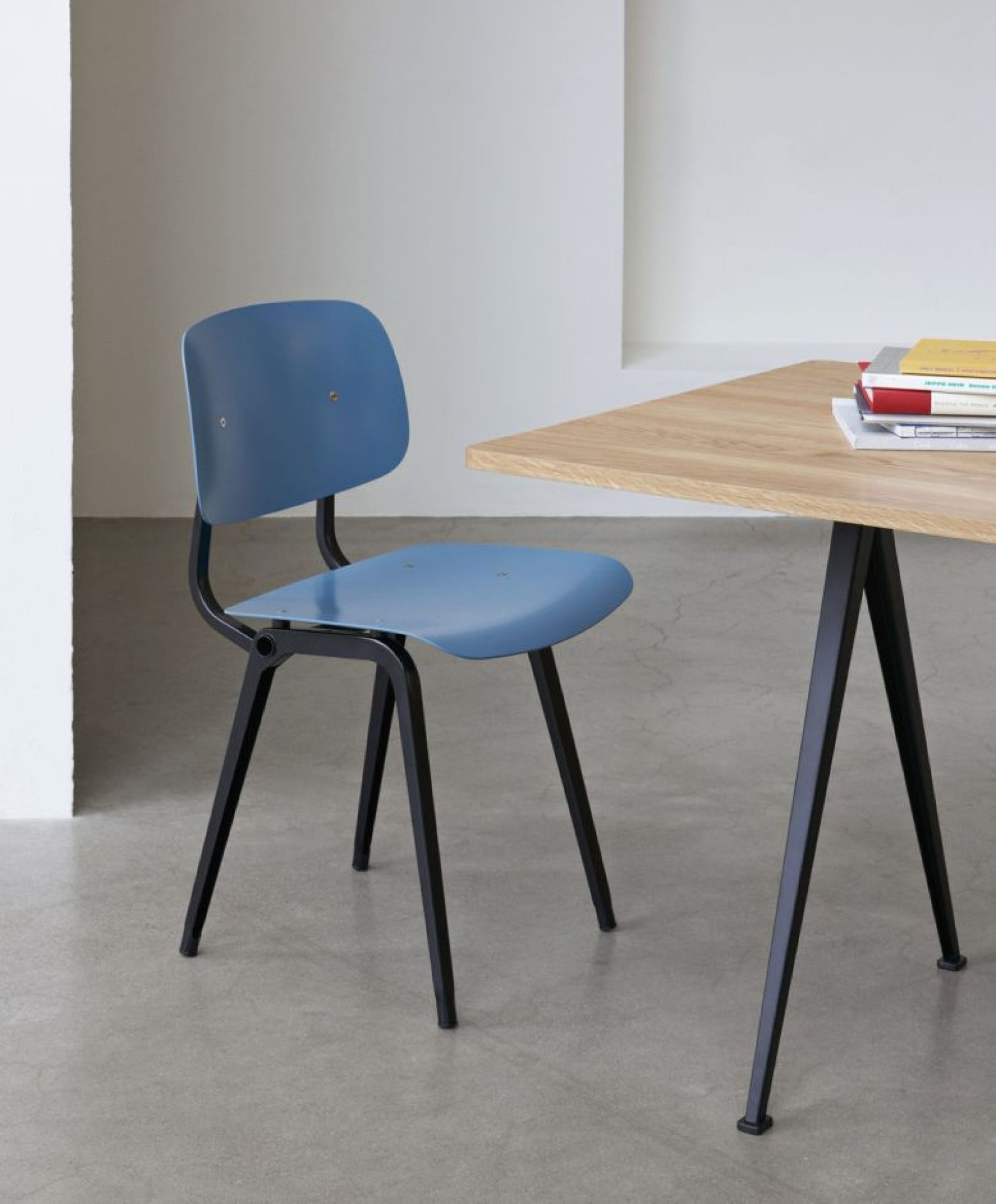 Blauer Hay Revolt Chair Stuhl mit schwarzem Gestell neben einem Holztisch im minimalistischen Design.