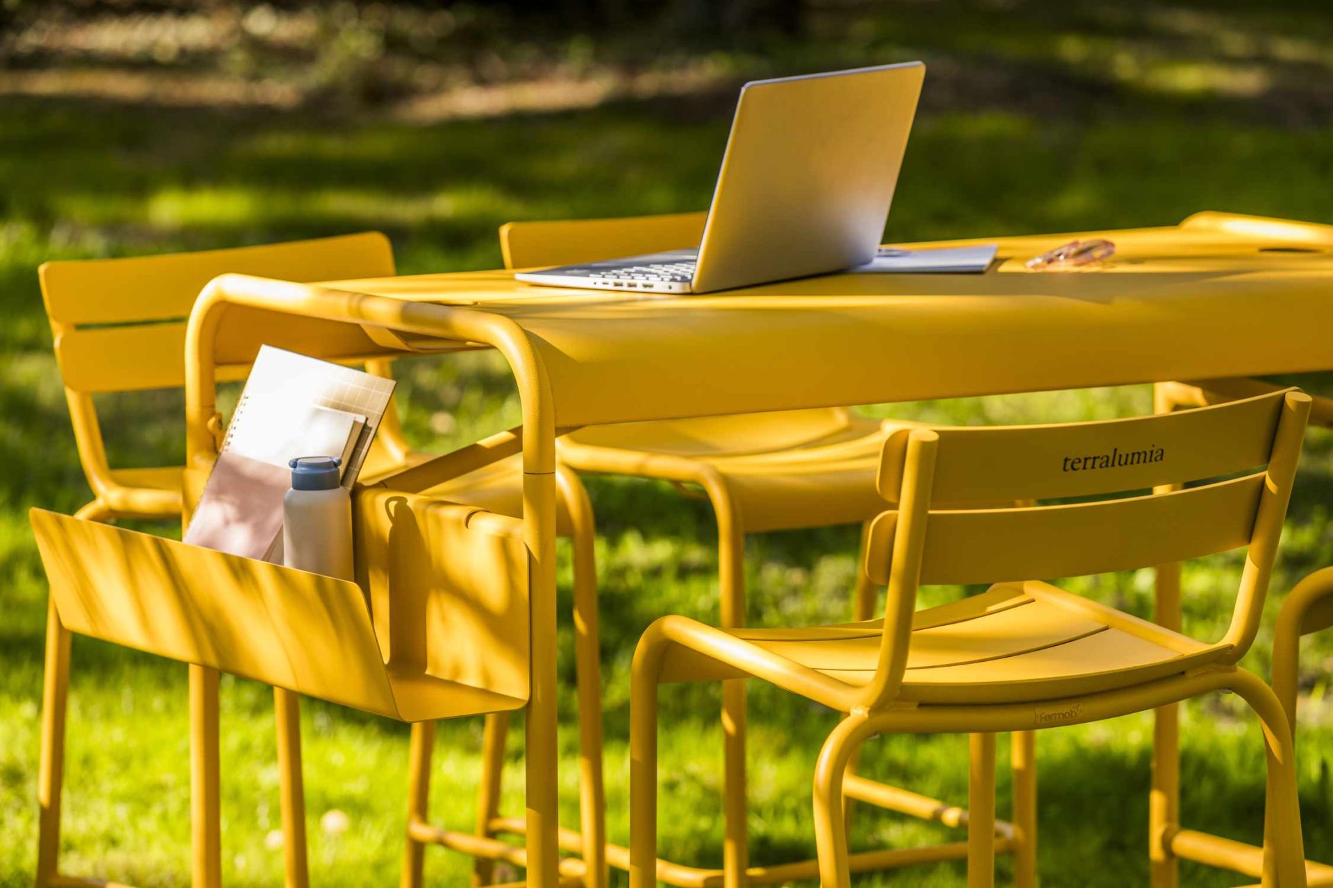 Gelber Luxembourg Work Stehtisch von Fermob im Freien mit Laptop und Arbeitsmaterialien.
