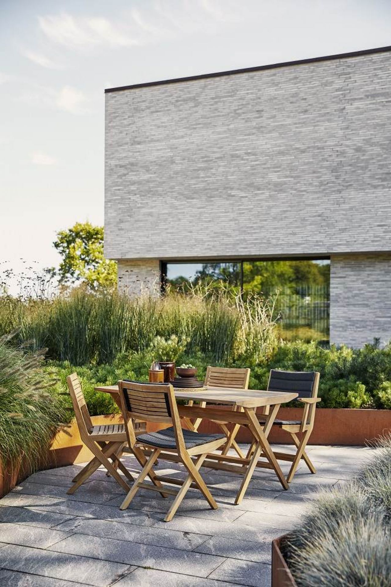 Cane-Line Flip Outdoor Stuhl 2er Set aus Teakholz mit grauen Sitzkissen auf Terrasse.