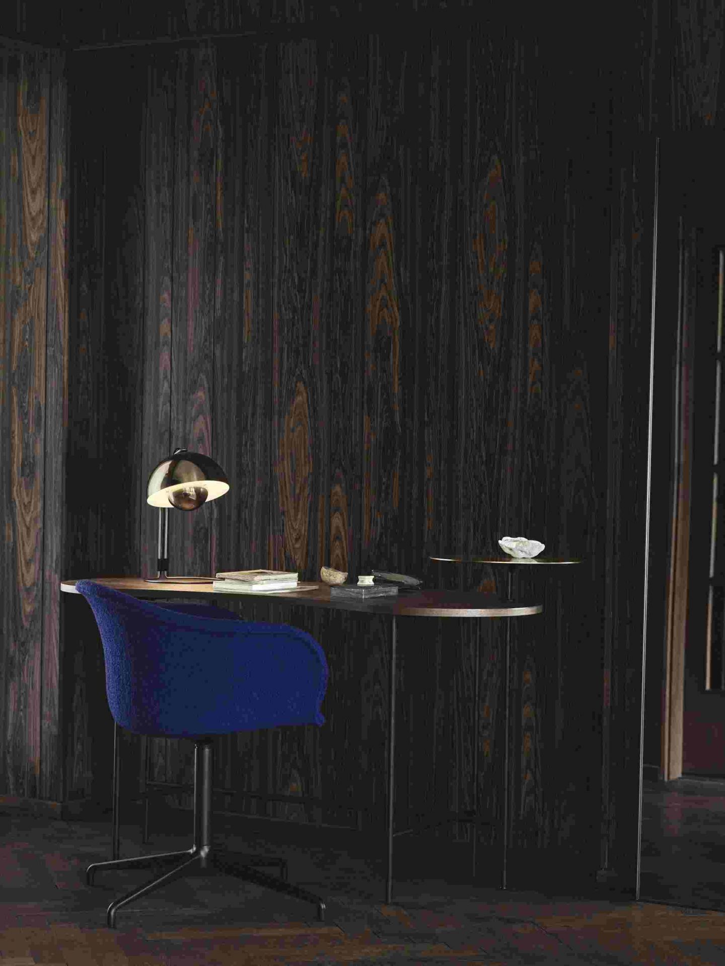 AndTradition Palette JH9 Schreibtisch mit Lampe und blauem Bürostuhl vor dunkler Holzvertäfelung.