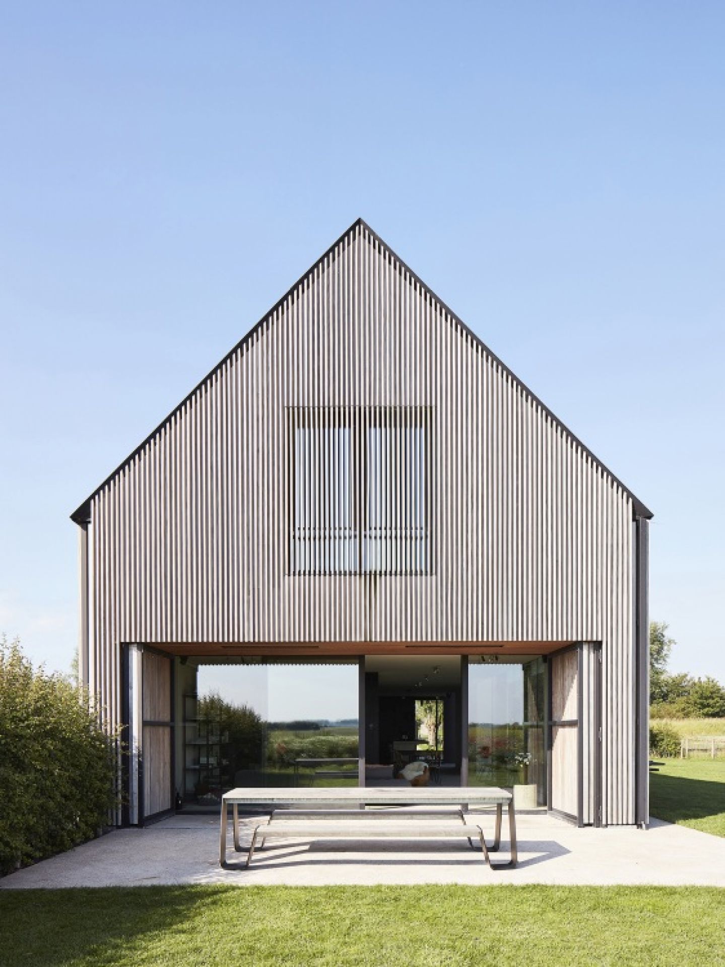 Extremis Hopper Picknickbank aus Holz und Metall im Außenbereich vor modernem Haus mit Glasfront.