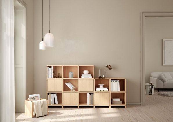 Heller Wohnraum mit Holzregal und Blick auf ein Wohnzimmer mit Sofa und Woud Teppich.
