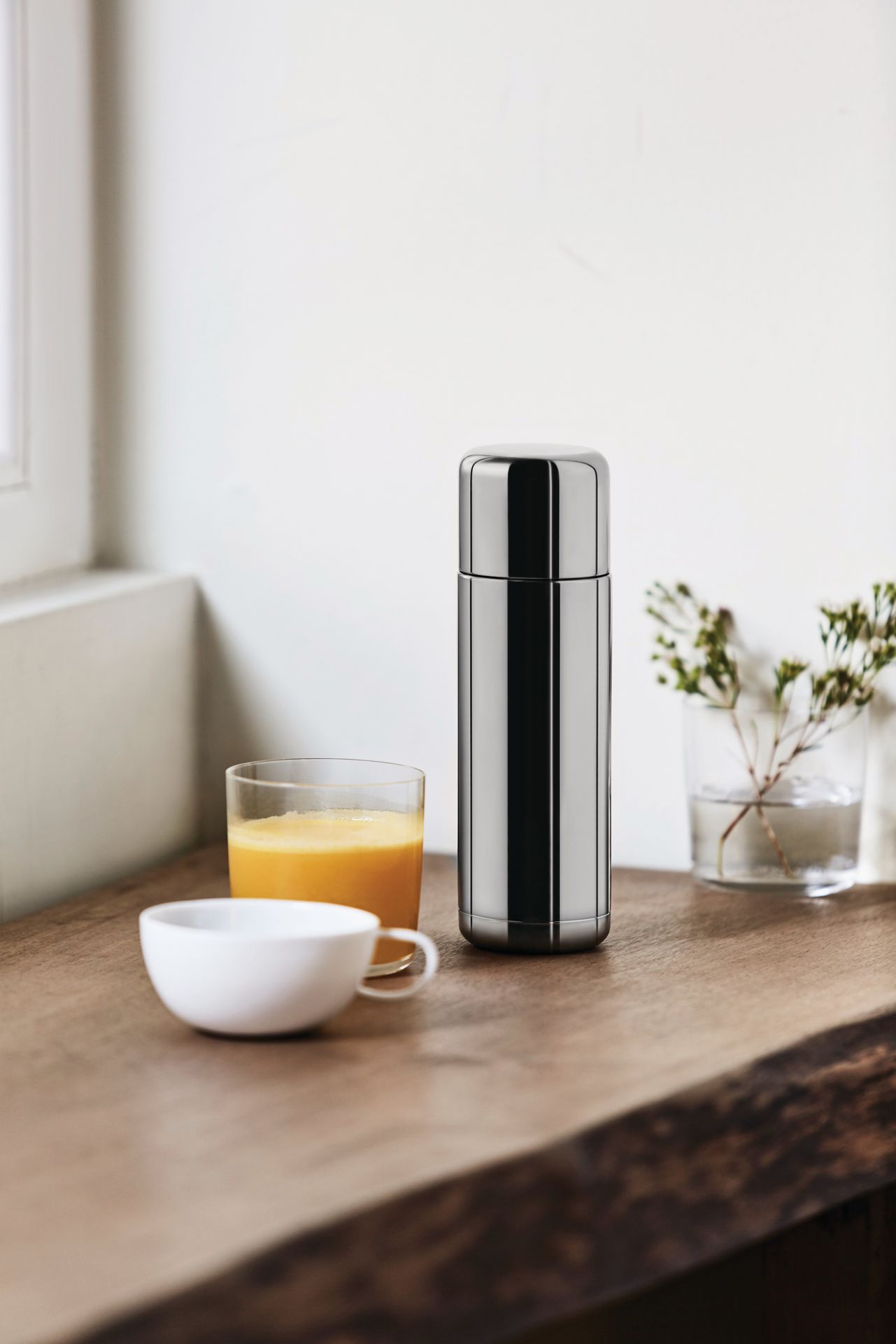 Nahaufnahme der Nomu Isolierkanne von Alessi, aus Edelstahl, neben Saft und Tasse.