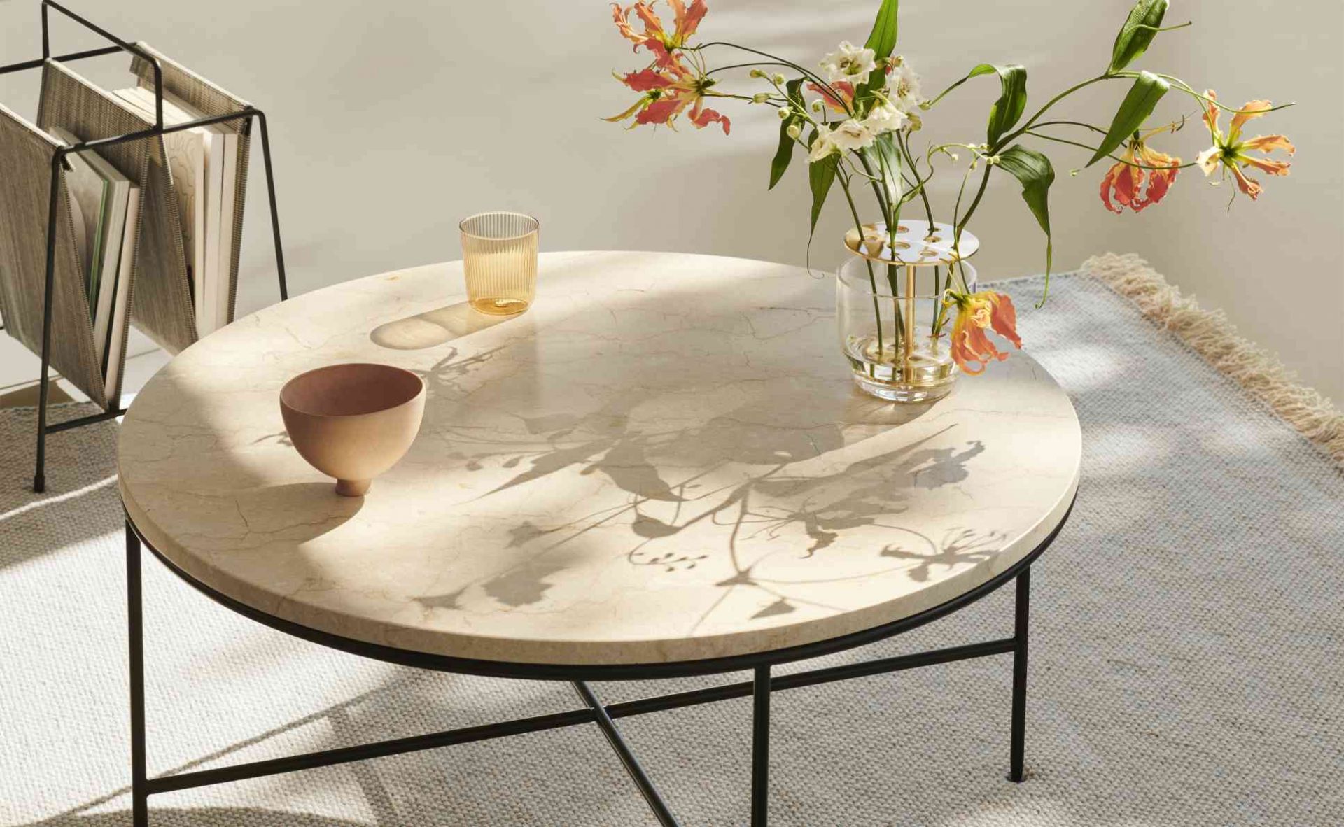 Fritz Hansen Planner Couchtisch aus Marmor mit Blumen, Schale und Glas auf einem Teppich.