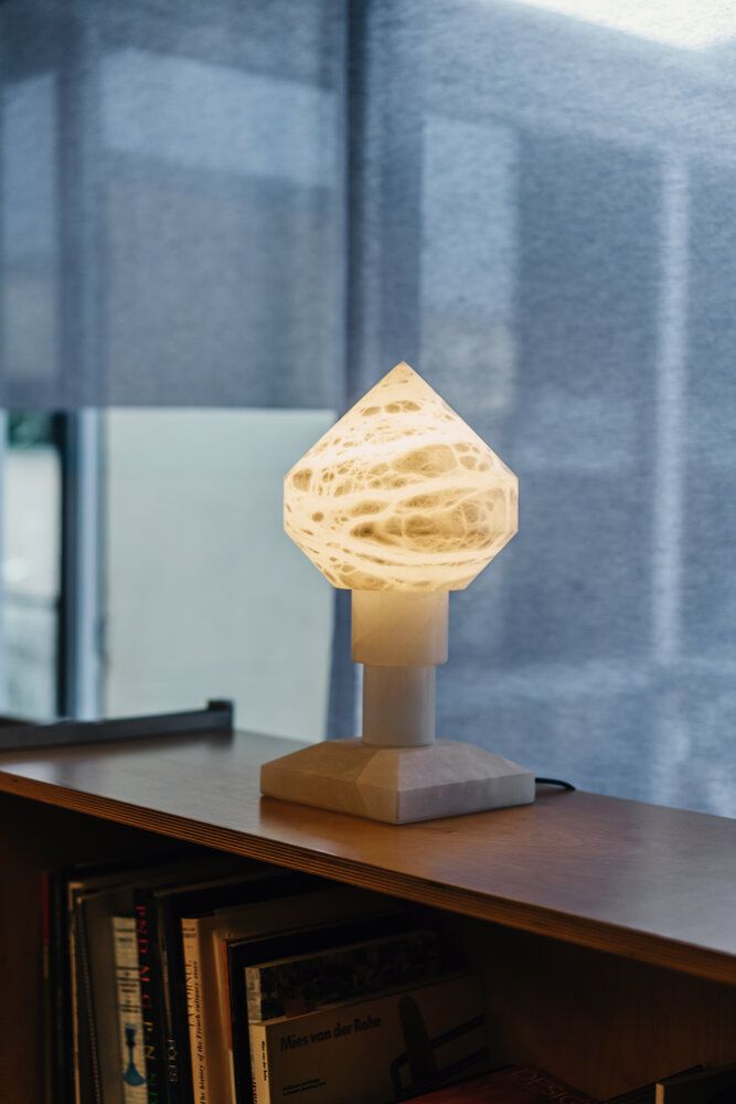Nahaufnahme der leuchtenden Zeleste Tischlampe von Santa & Cole auf einem Holzregal.