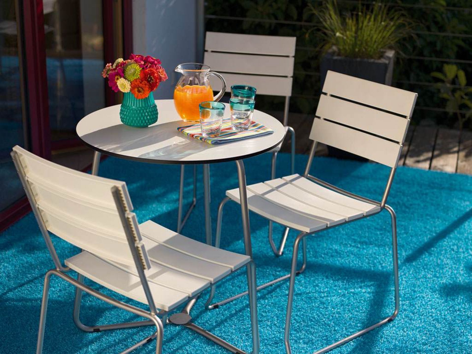 Weishäupl Bistrotisch: Runder Gartentisch mit Edelstahlgestell und passenden Stühlen auf einem sonnigen Balkon.