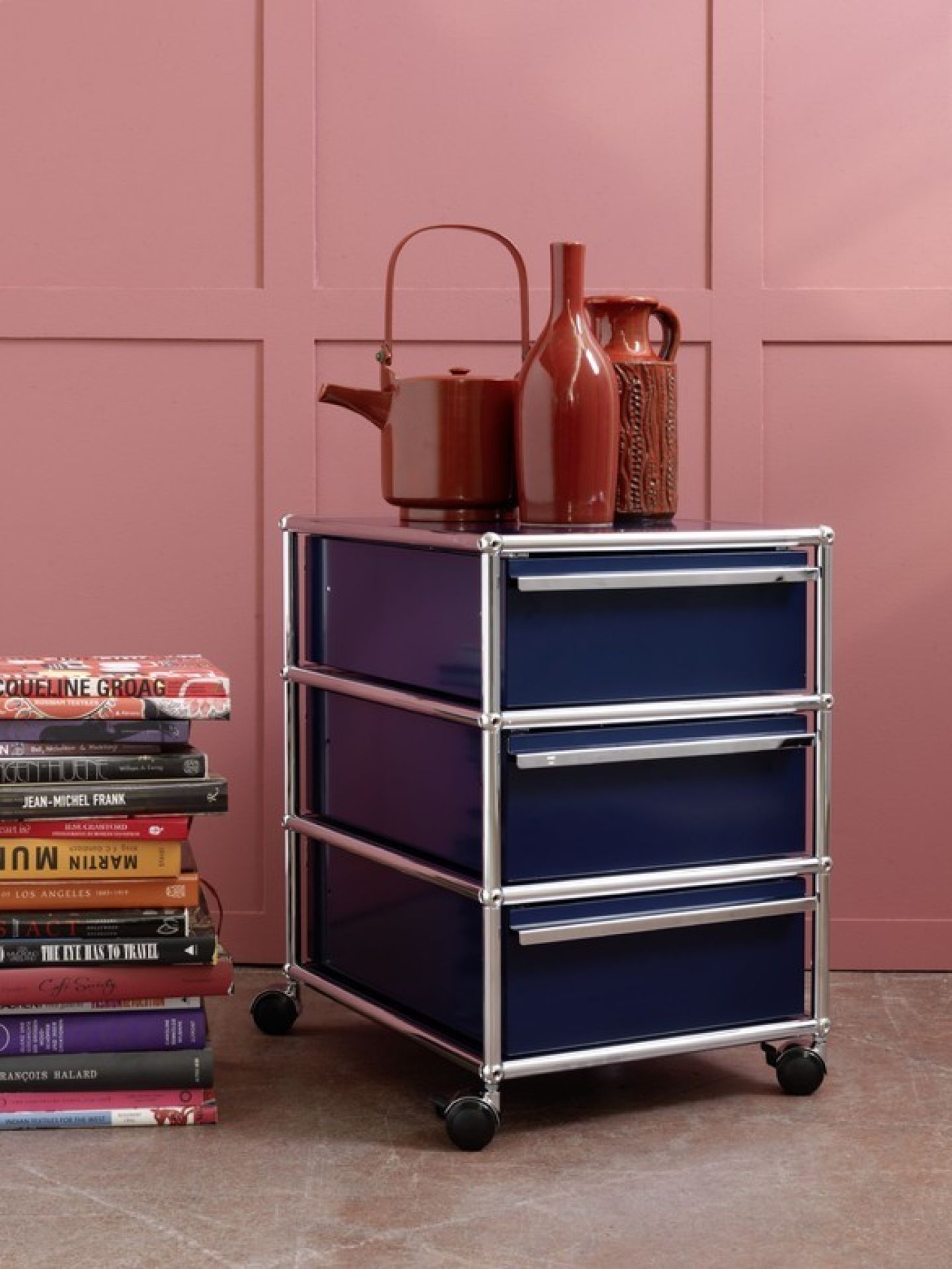 USM Haller Rollcontainer in Enzianblau mit drei Schubladen und Chromgestell, auf dem Vasen stehen.