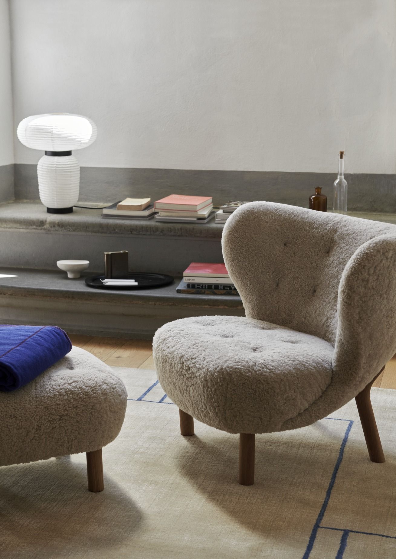 AndTradition Teppich Cruise AP11 in Beige mit blauem Muster unter Sessel und Hocker.