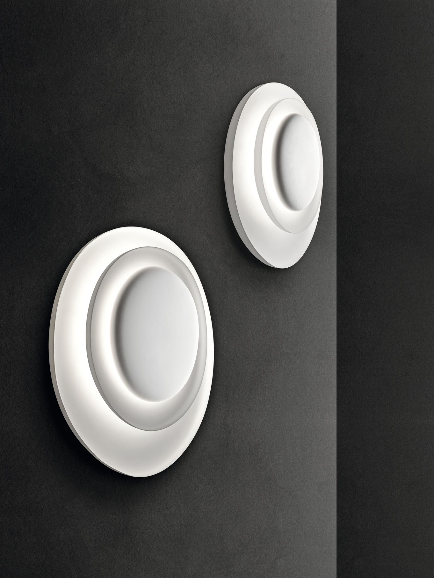 Zwei moderne, runde Bahia Wandleuchten von Foscarini in Weiß an einer dunklen Wand.