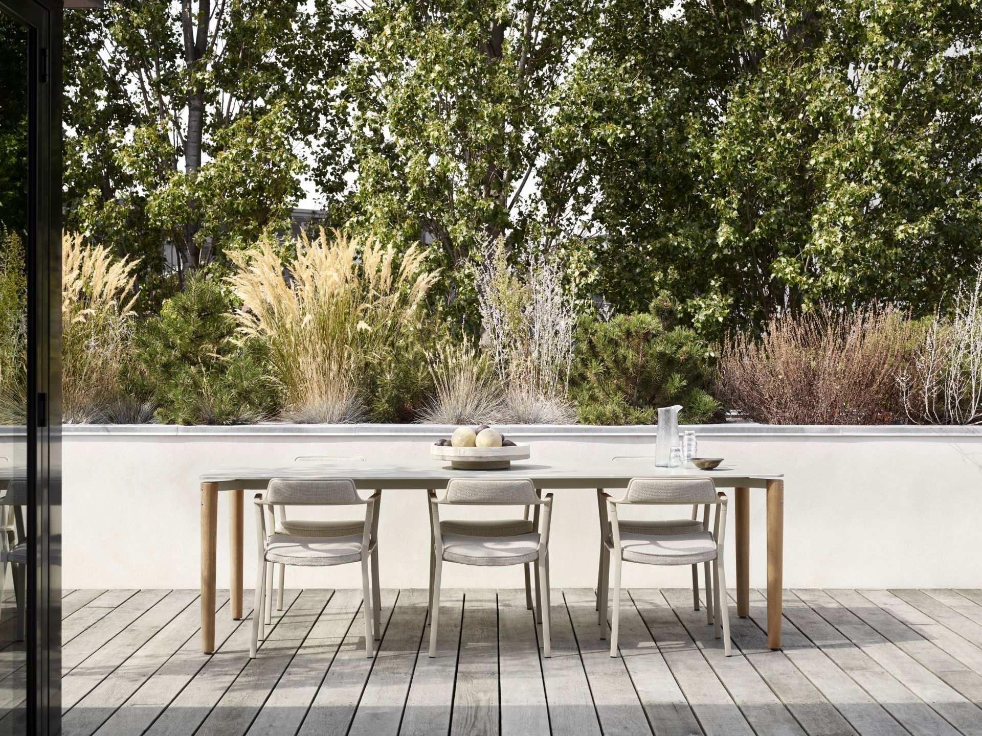 Vipp Open-Air Outdoor Stühle und Esstisch auf einer Terrasse mit Holzboden und grüner Bepflanzung.