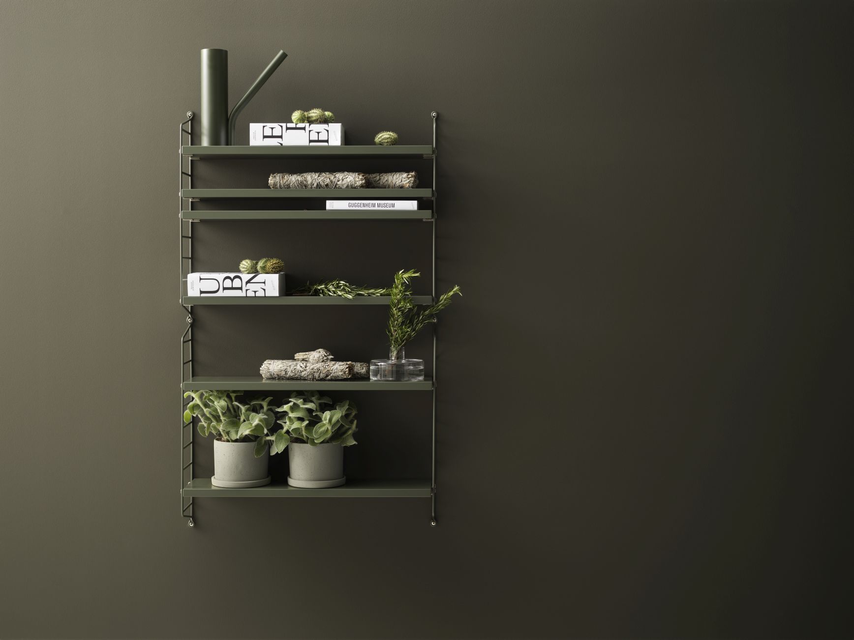 Blaues String Pocket Regal aus Metall mit Deko-Elementen an einer dunklen Wand.