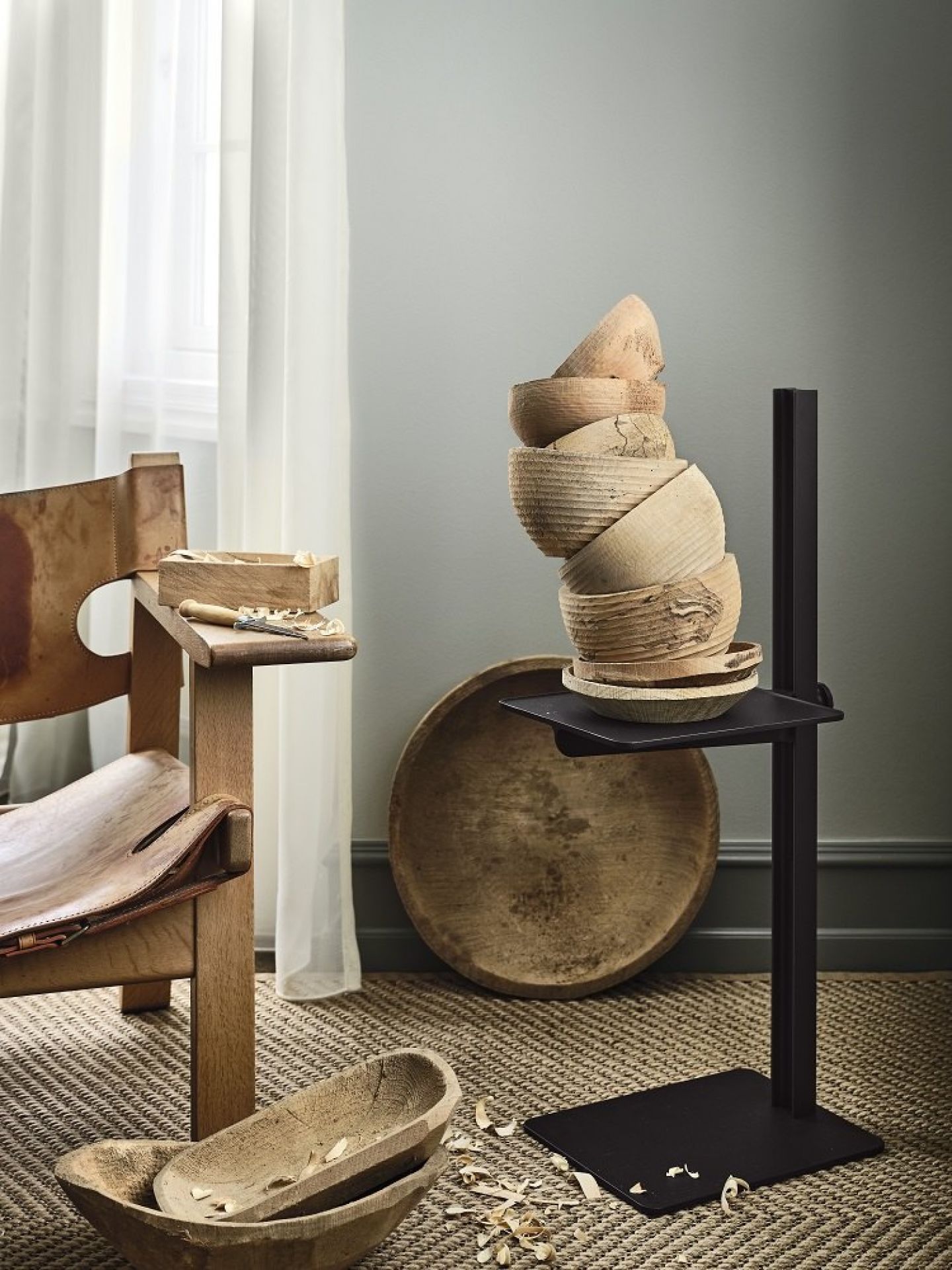 Schwarzer, höhenverstellbarer Museum Sidetable Beistelltisch von String Furniture mit Holzschalen dekoriert, neben einem Holzstuhl.