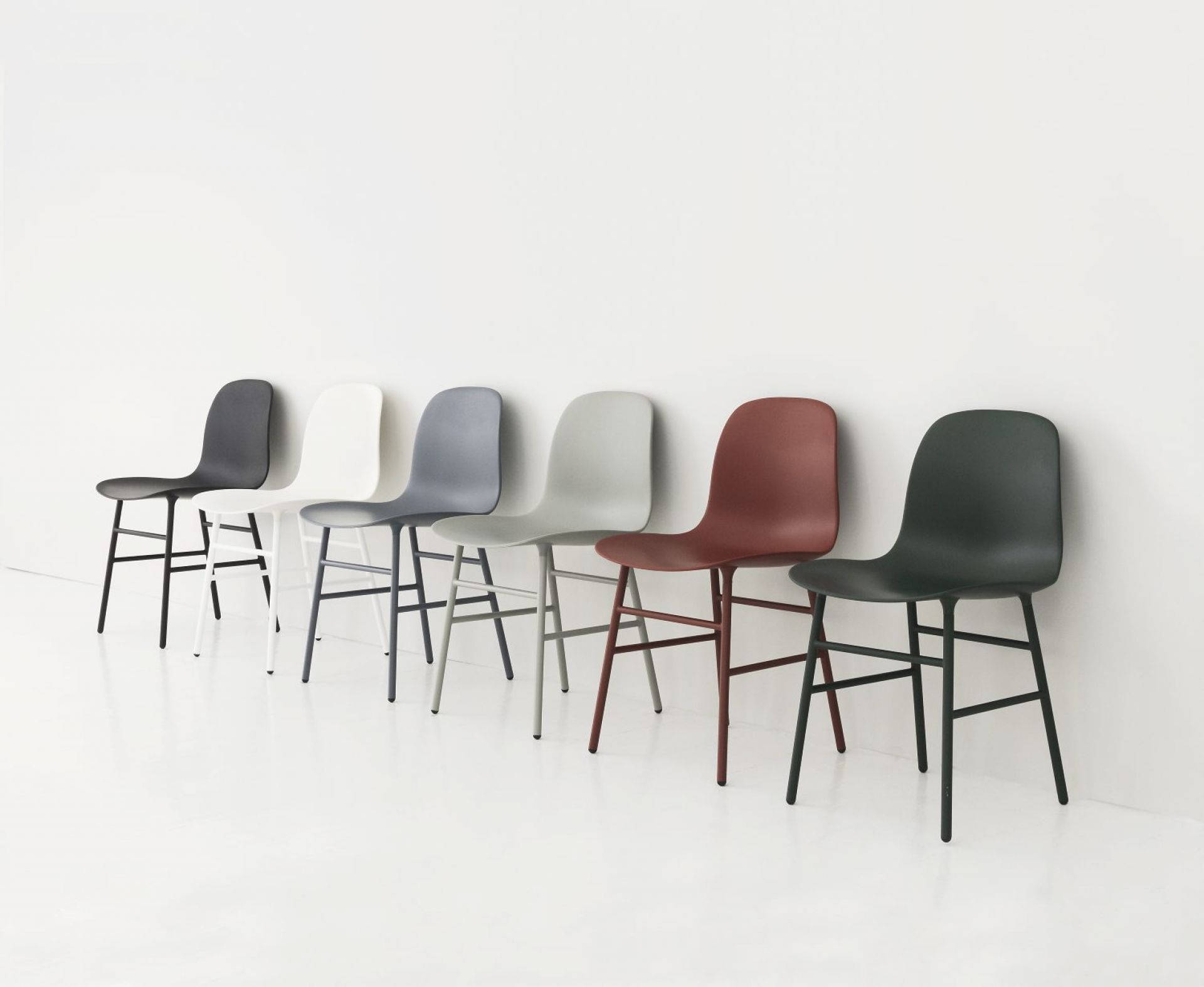 Reihe von Form Stühlen von Normann Copenhagen in verschiedenen Farben vor einer weißen Wand.