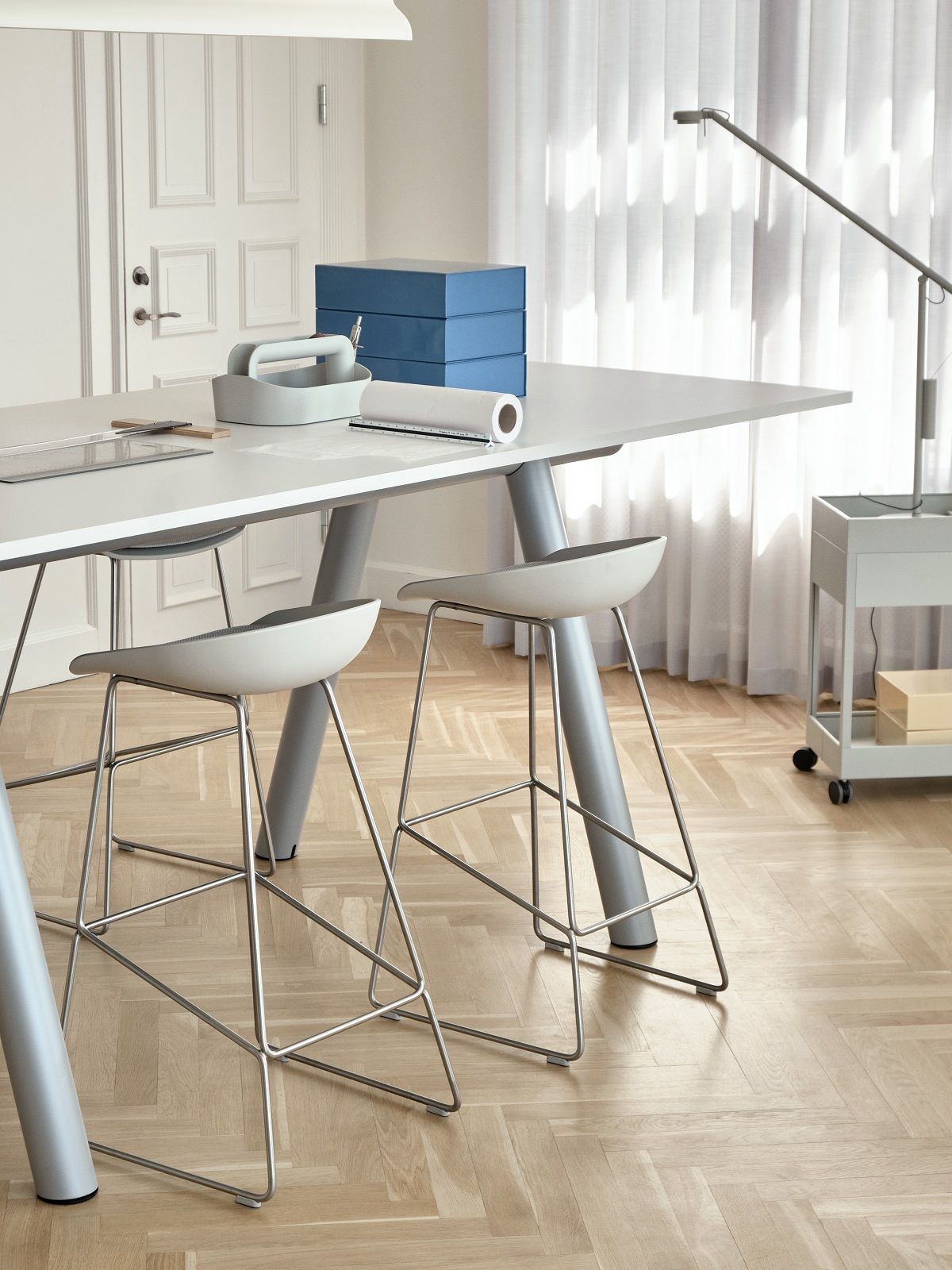 Heller Boa Table Tisch von Hay mit zwei Barhockern und Büro-Accessoires auf einem Parkettboden.