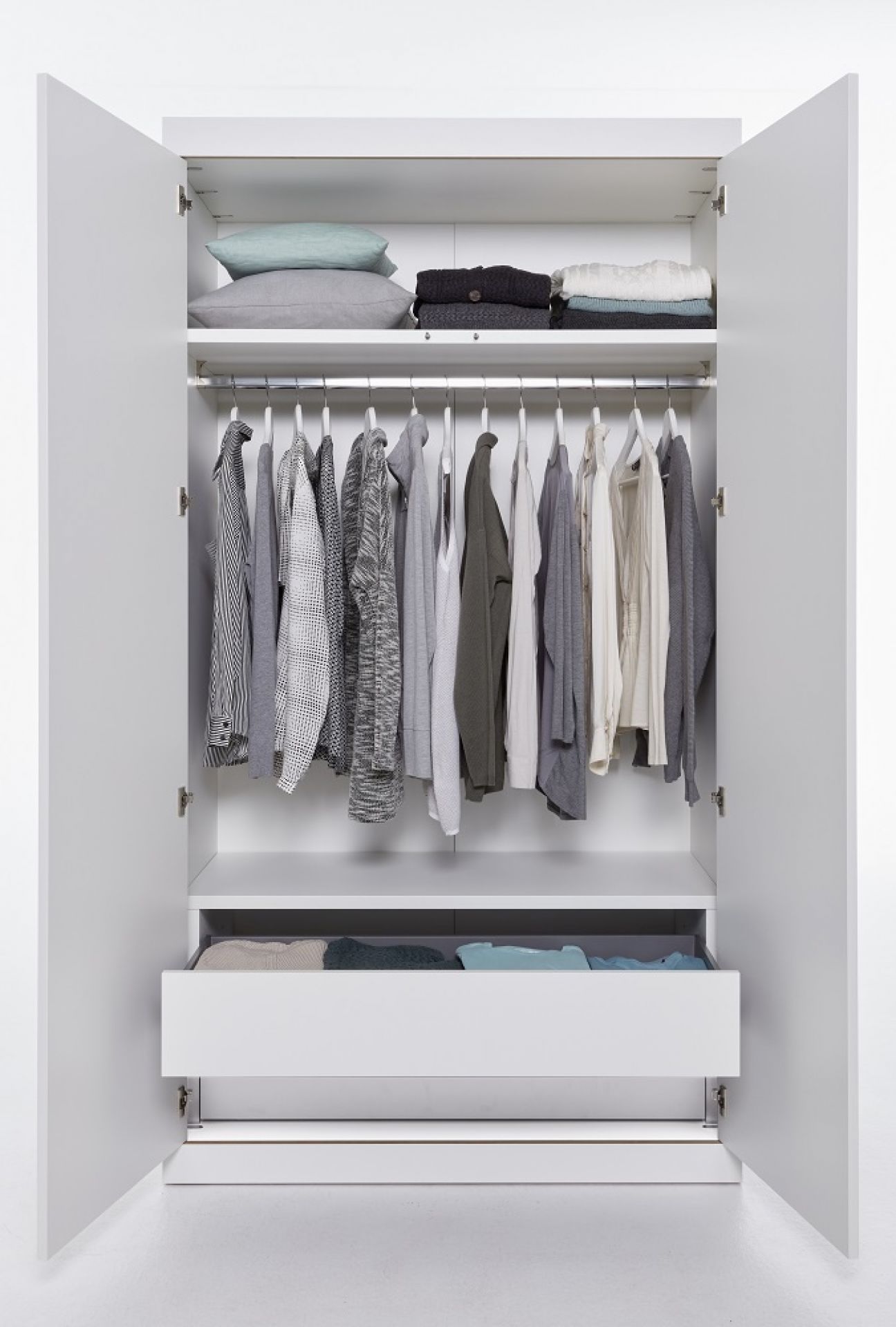 Offener, weißer Flai Kleiderschrank von Müller Möbelwerkstätten mit Kleidung, Kissen und Schublade.