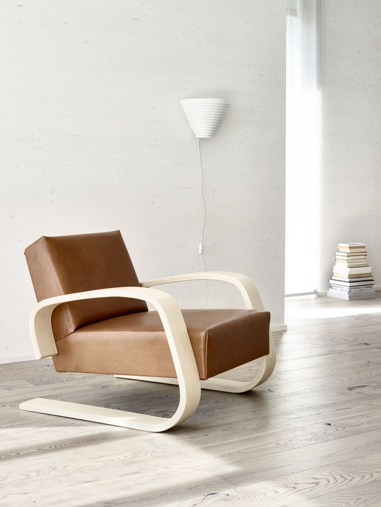 A910 Wandleuchte von Artek in weiß über einem braunen Sessel mit hellem Holzgestell.