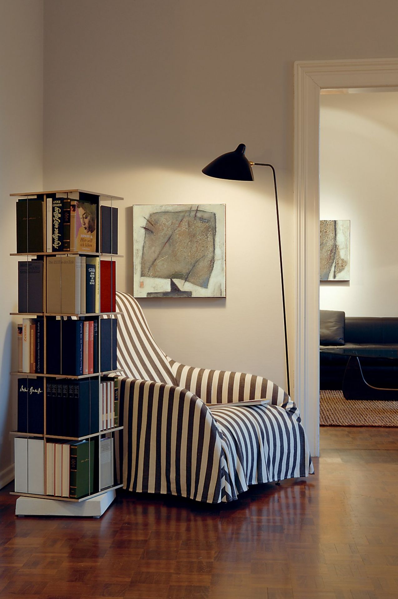 Nils Holger Moormann Buchstabler Bücherregal neben Sessel mit Streifenmuster und Stehlampe in modernem Wohnzimmer.