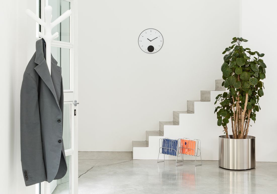 Helle Raumansicht mit Rexite Wanduhr, Treppe, Pflanze und Garderobe. Moderne Einrichtung.