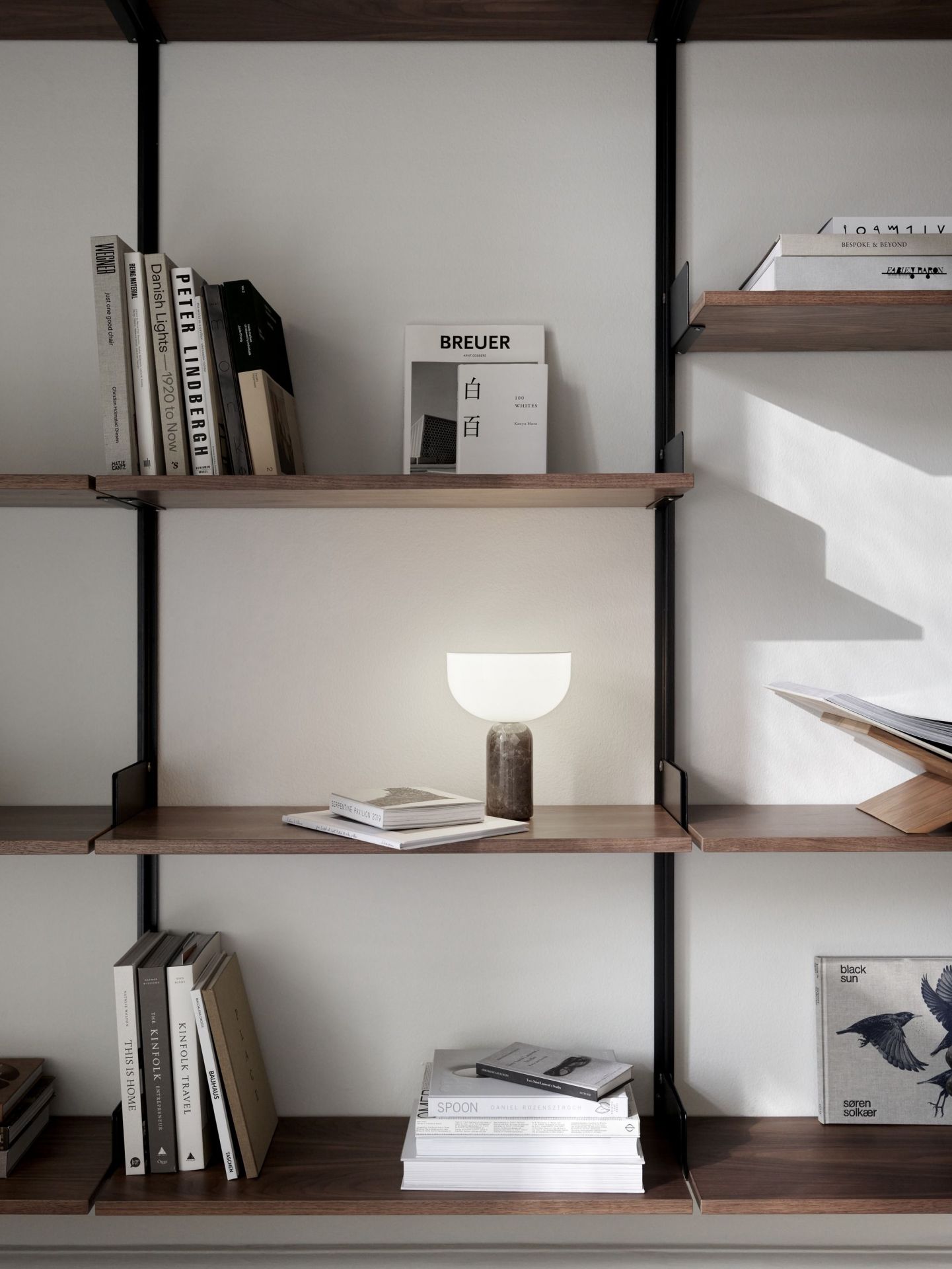 New Works Kizu Tischleuchte auf Regal mit Büchern, modernes Design, stimmungsvolle Beleuchtung.