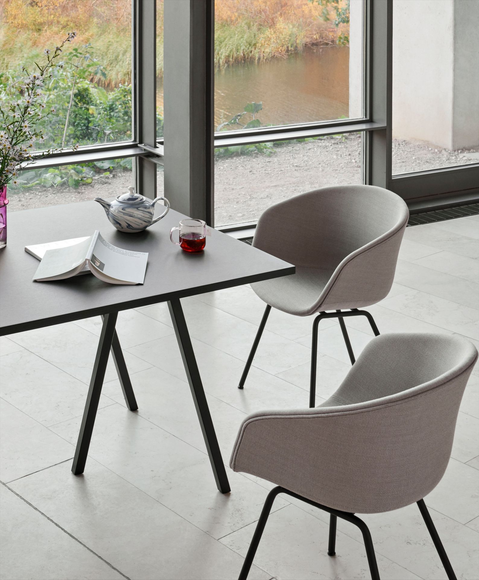 Zwei About A Chair AAC27 Stühle mit grauem Vollpolster und schwarzem Stahlgestell an Esstisch.