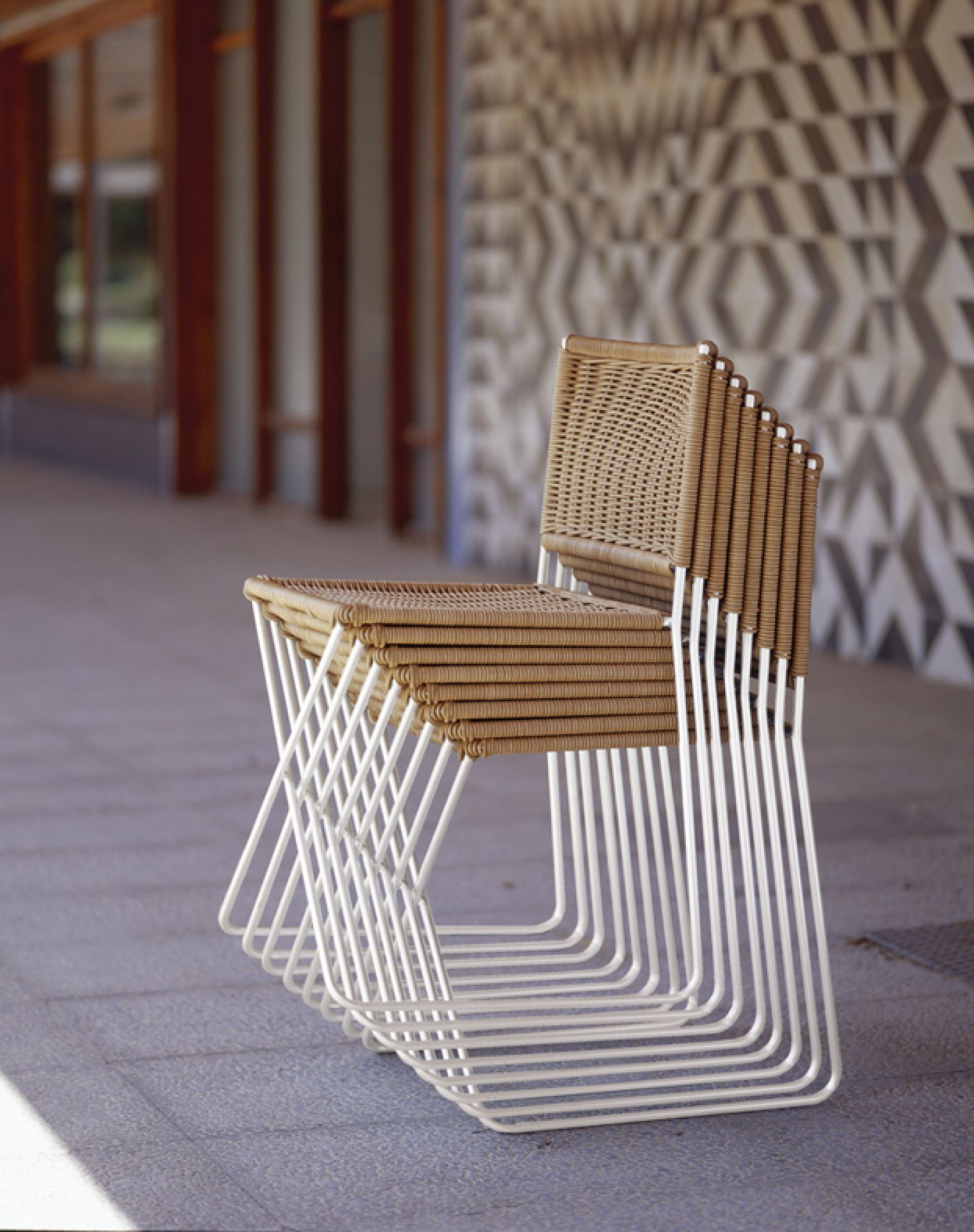 Gestapelte Ramón Rattanstühle von Santa & Cole mit weißem Metallgestell und Rattan-Sitzfläche.