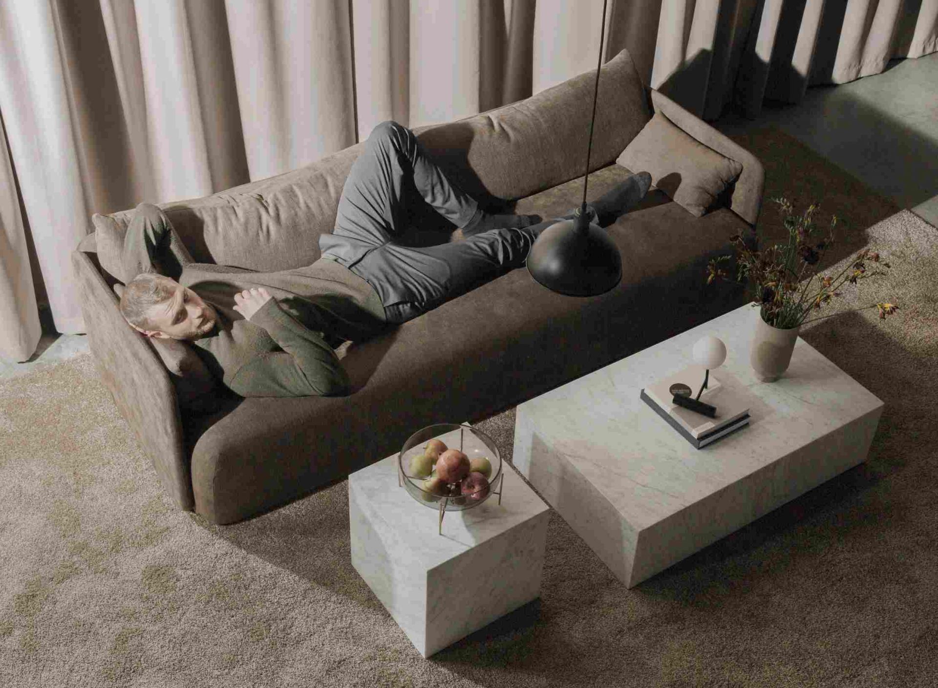 Mann entspannt auf Sofa neben Audo Copenhagen Plinth Tisch aus Marmor, minimalistisches Wohnzimmer Design.