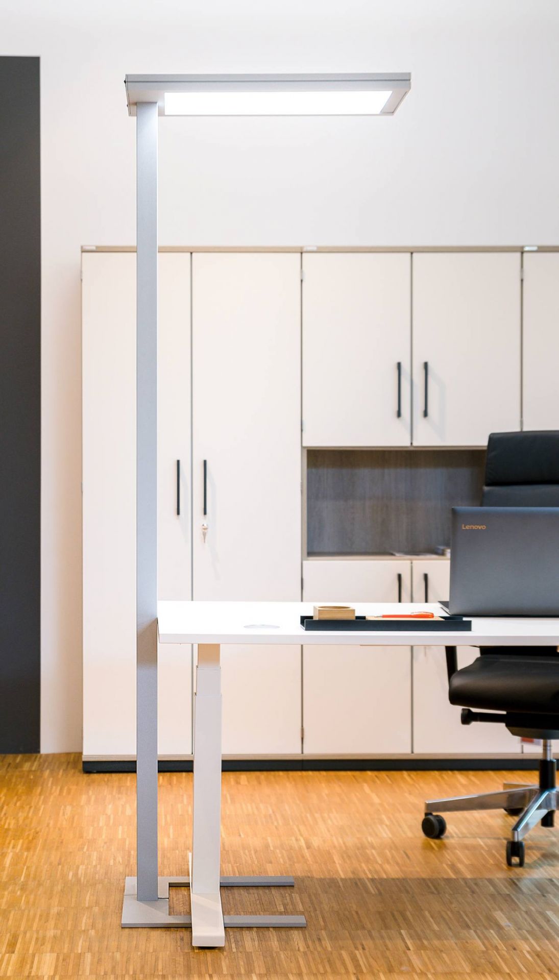 Hiplift Sitz-Stehtisch: Elektrisch höhenverstellbarer Schreibtisch mit Büromöbeln und Laptop im modernen Büro.