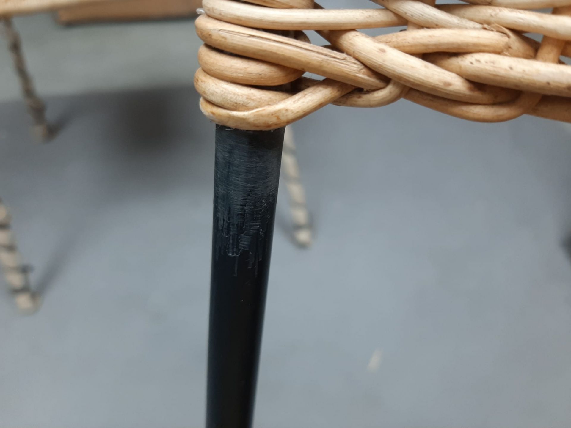 Detailaufnahme eines Richard Lampert Stuhls mit schwarzem Metallbein und geflochtener Sitzfläche aus Rattan.