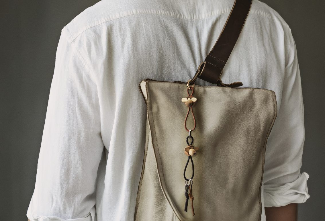 Nahaufnahme einer Person mit einer Tasche, an der ein Kay Bojesen Affe Schlüsselanhänger aus Holz hängt.