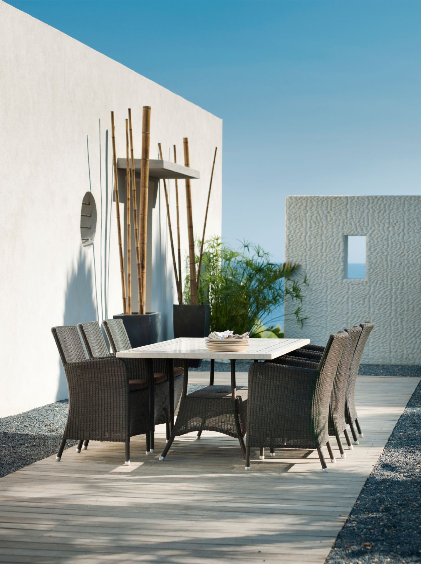 Cane-Line Hampsted Gartensessel und Esstisch aus Rattan auf einer Holzterrasse mit modernem Hintergrund.