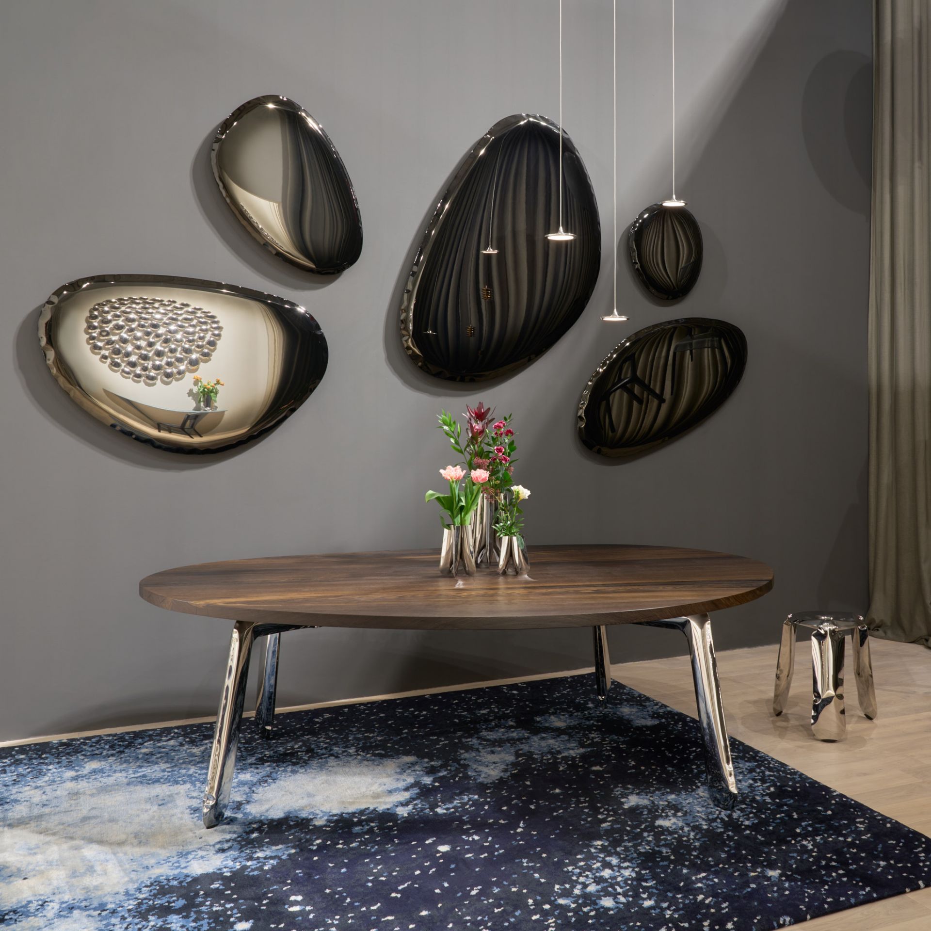 Raumansicht mit Tafla Spiegeln von Zieta in Dark Matter, Holztisch mit Blumen und blauem Teppich.