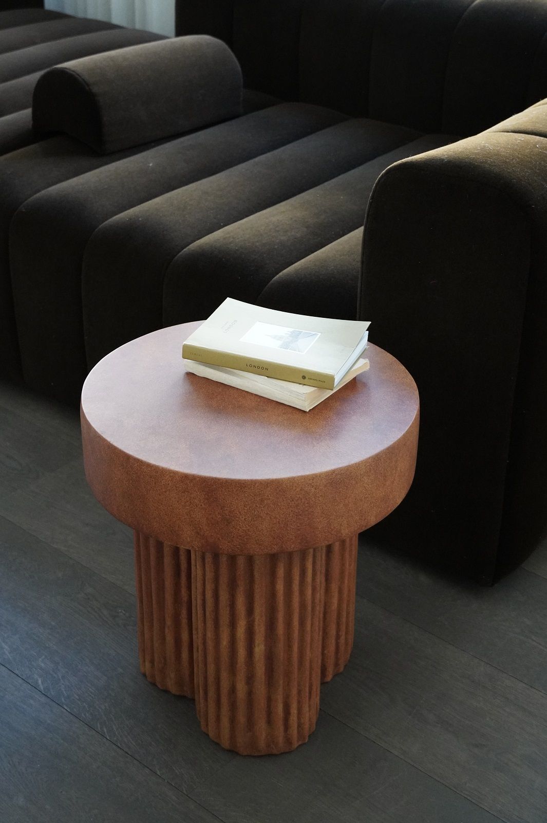 Nahaufnahme des Gear Tall Side Table von Norr11 in Terrakotta mit Büchern, neben einem dunklen Sofa.