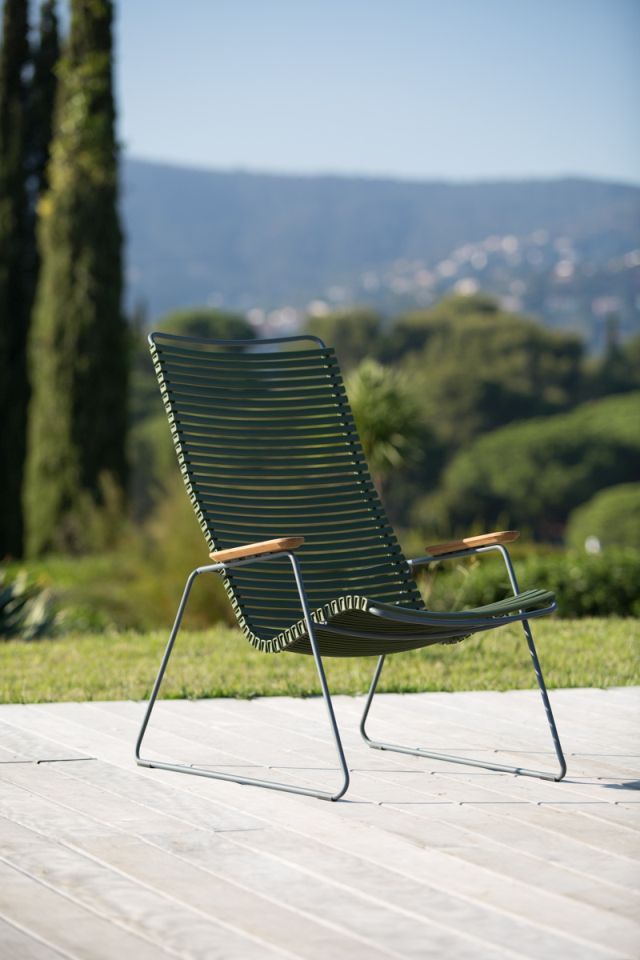 Dunkelgrauer Click Lounge Chair Sessel von Houe für den Außenbereich mit Holzarmlehnen vor grüner Landschaft.